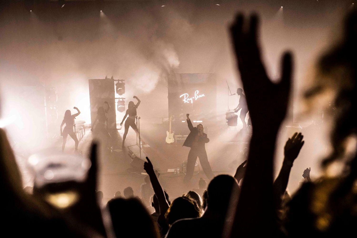 Silhouetted crowd at concert or event with hands raised against backlit foggy atmosphere. London Event Photographer