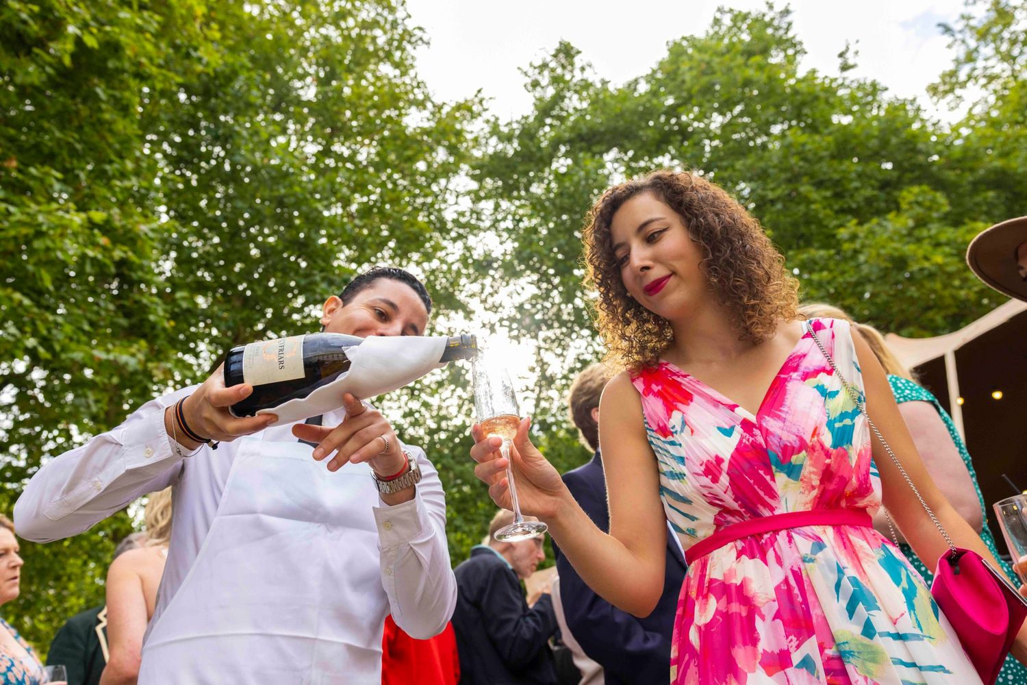 Group of people dancing and celebrating outdoors under green trees. London Event Photographer