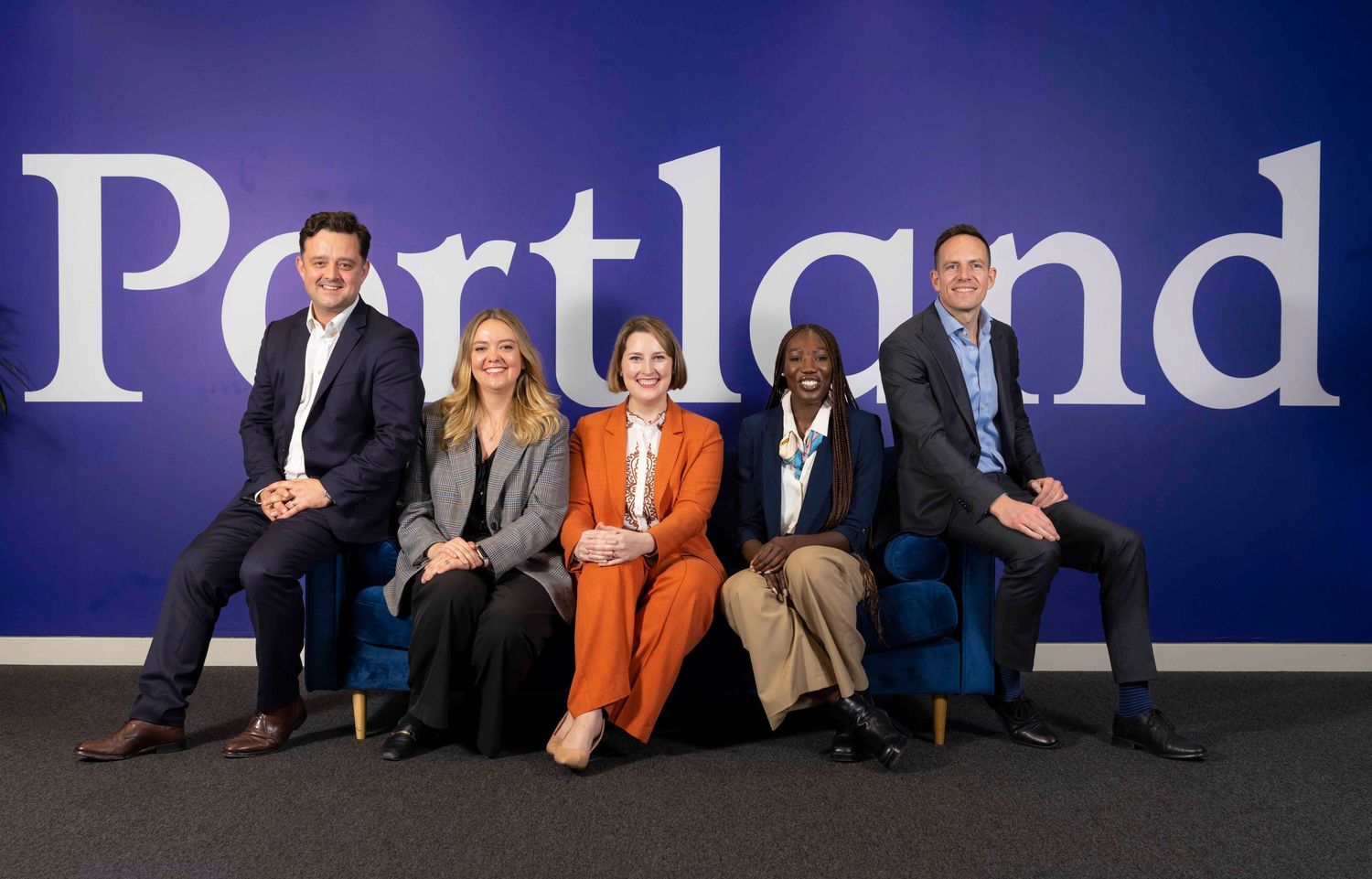 Row of people sitting against blue wall with text in corporate setting. London Event Photographer