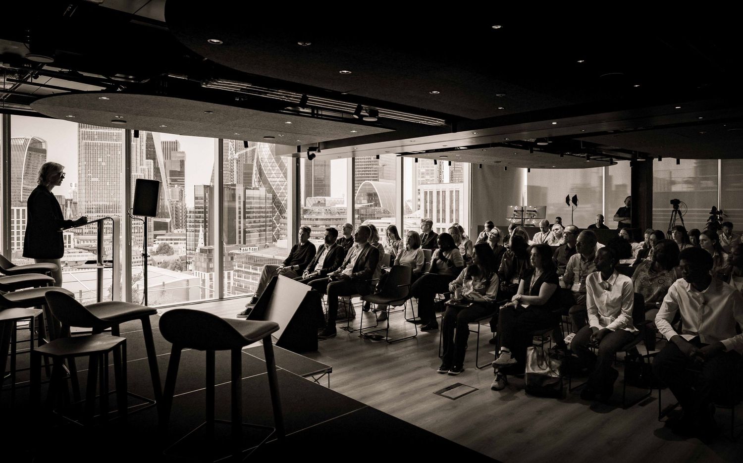 Silhouetted audience members seated in a darkened conference or presentation hall. London Event Photographer