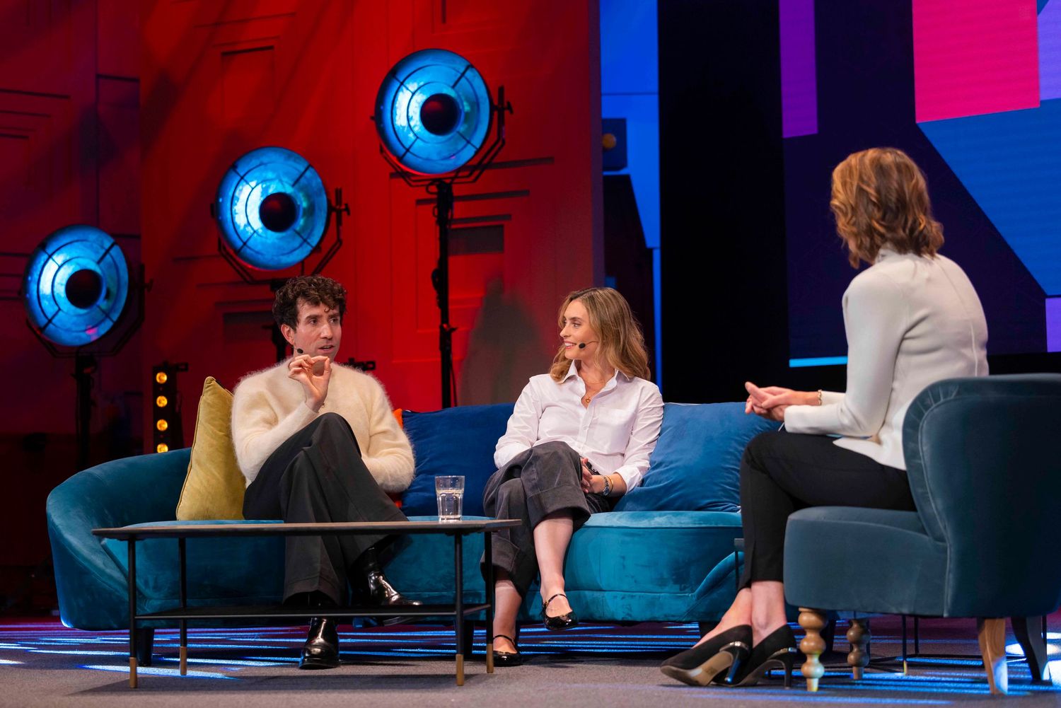 Three people engaged in conversation while seated on blue couch during televised interview at a london event. London Event Photographer