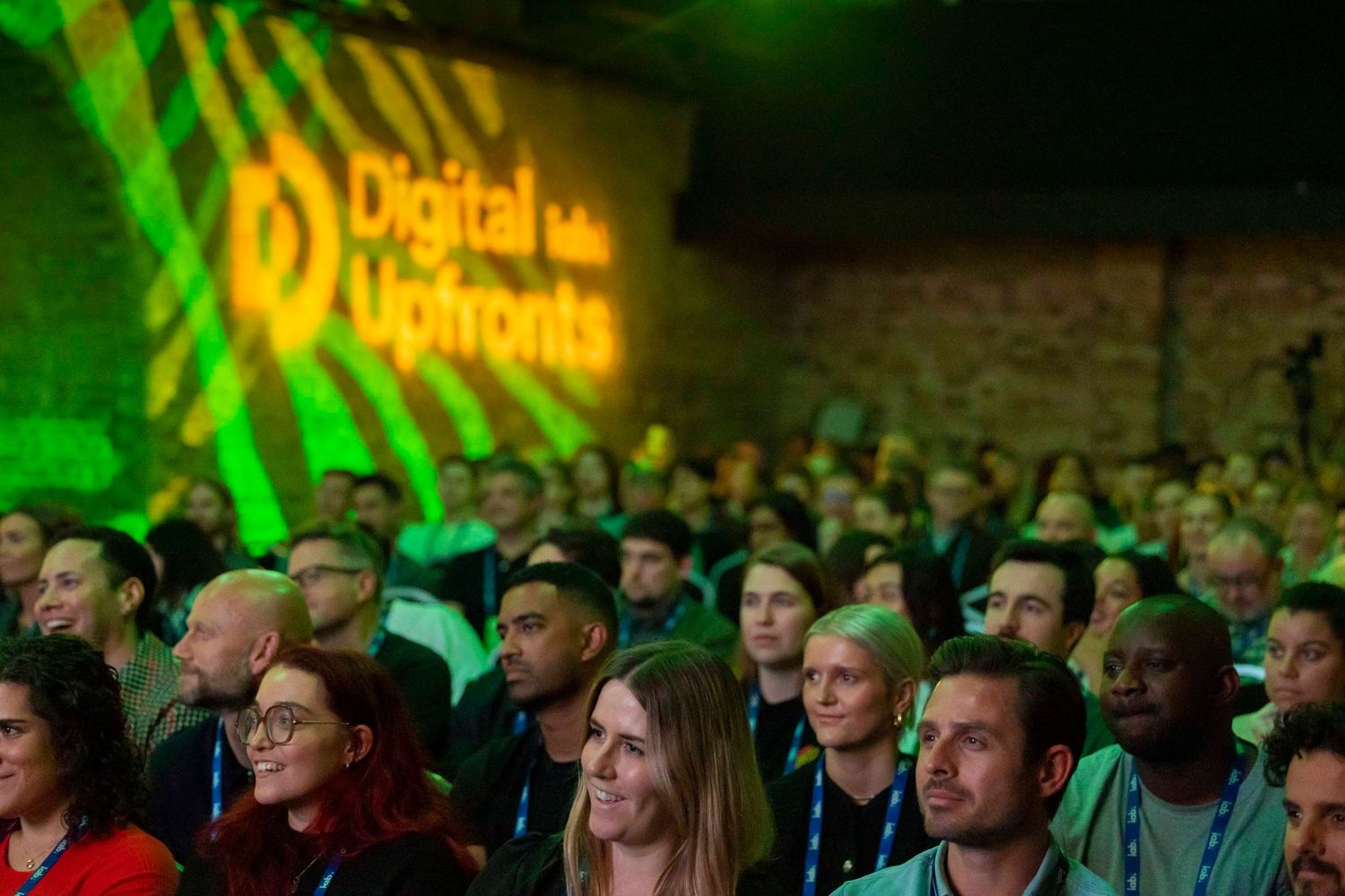 Large audience watching presentation in darkened venue with green and yellow lighting. London Event Photographer