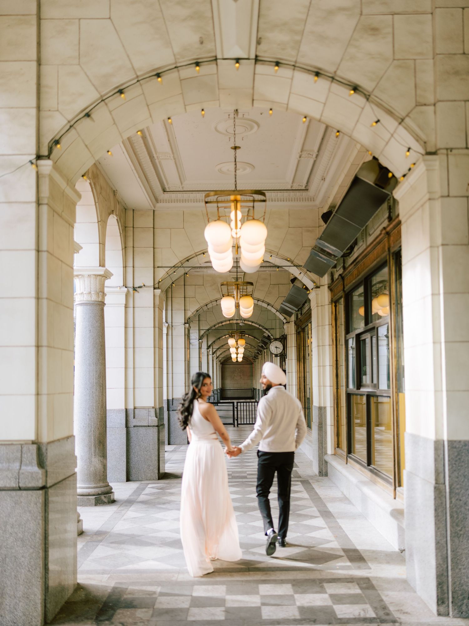 Couple strolls hand in hand through a stunning arched colonnade with checkered marble floors.