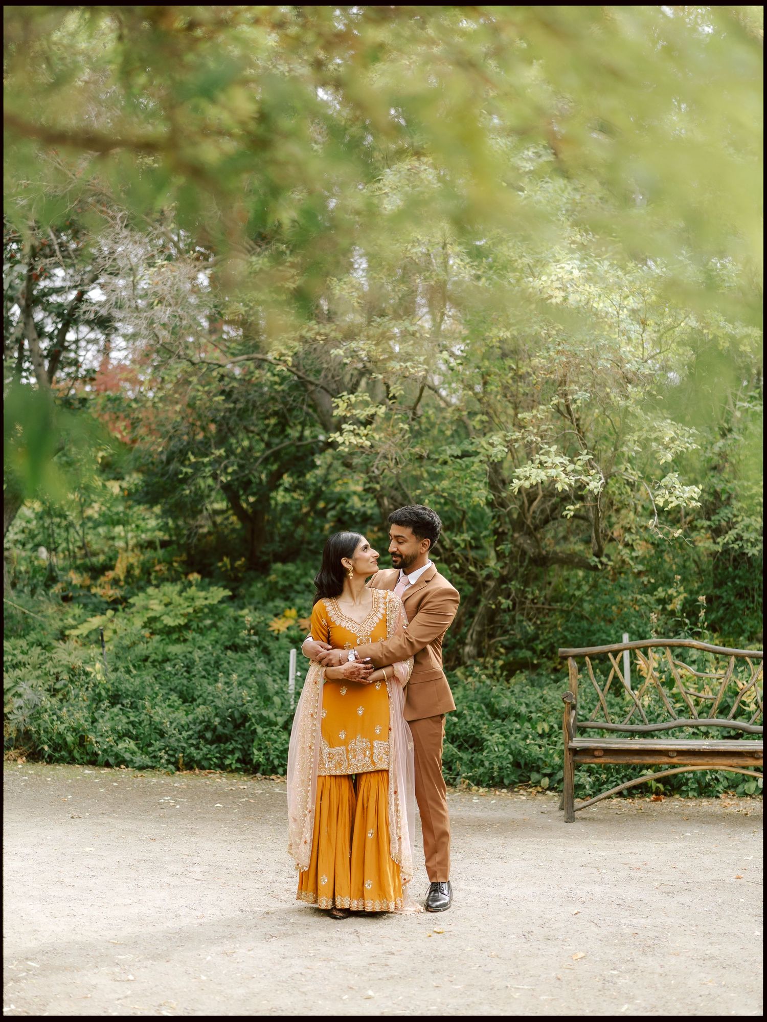 South Asian couple in traditional attire sharing a romantic moment in a lush garden setting.