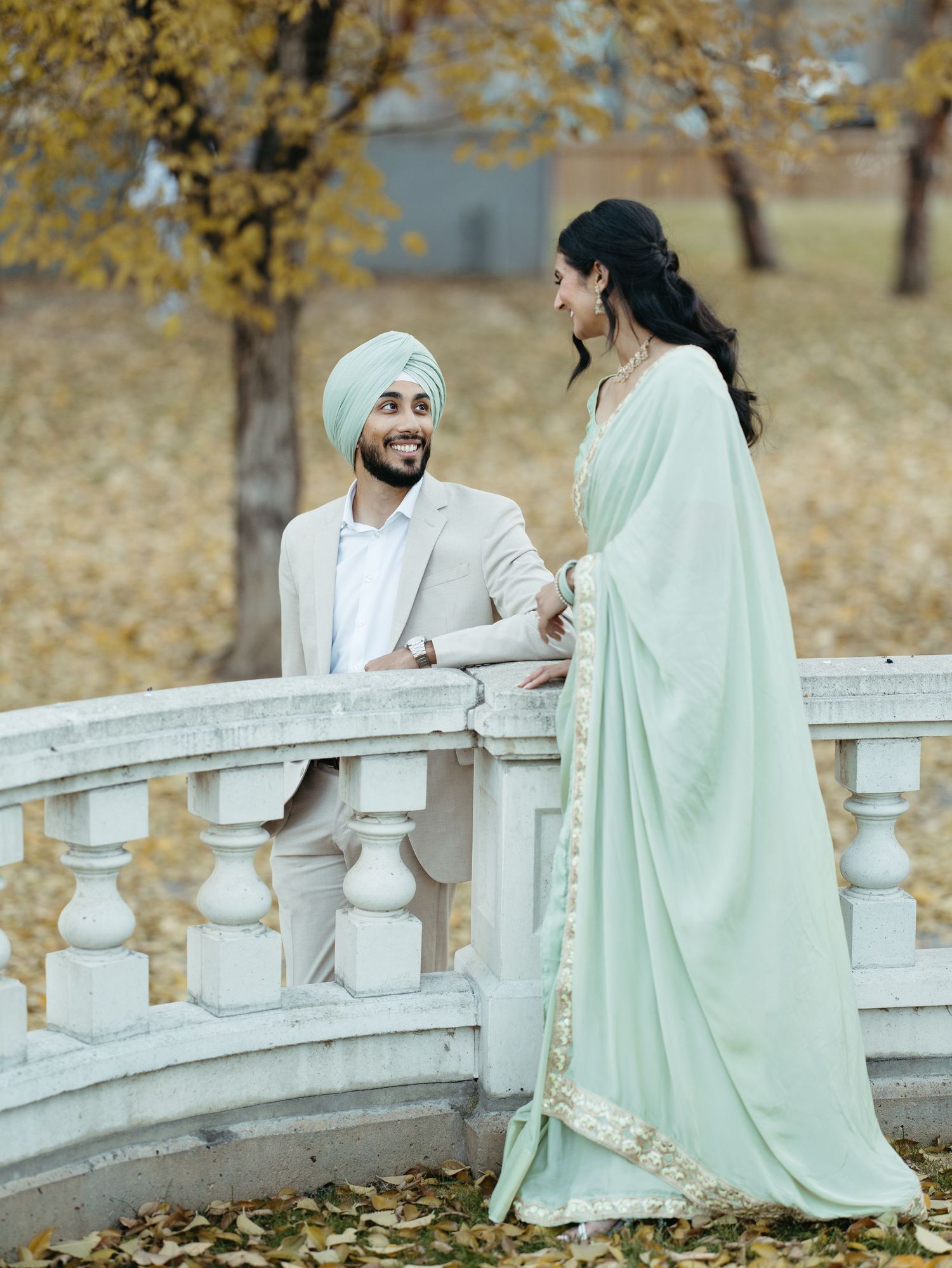 Sikh couple sharing a romantic moment on a white stone bridge surrounded by golden autumn leaves.