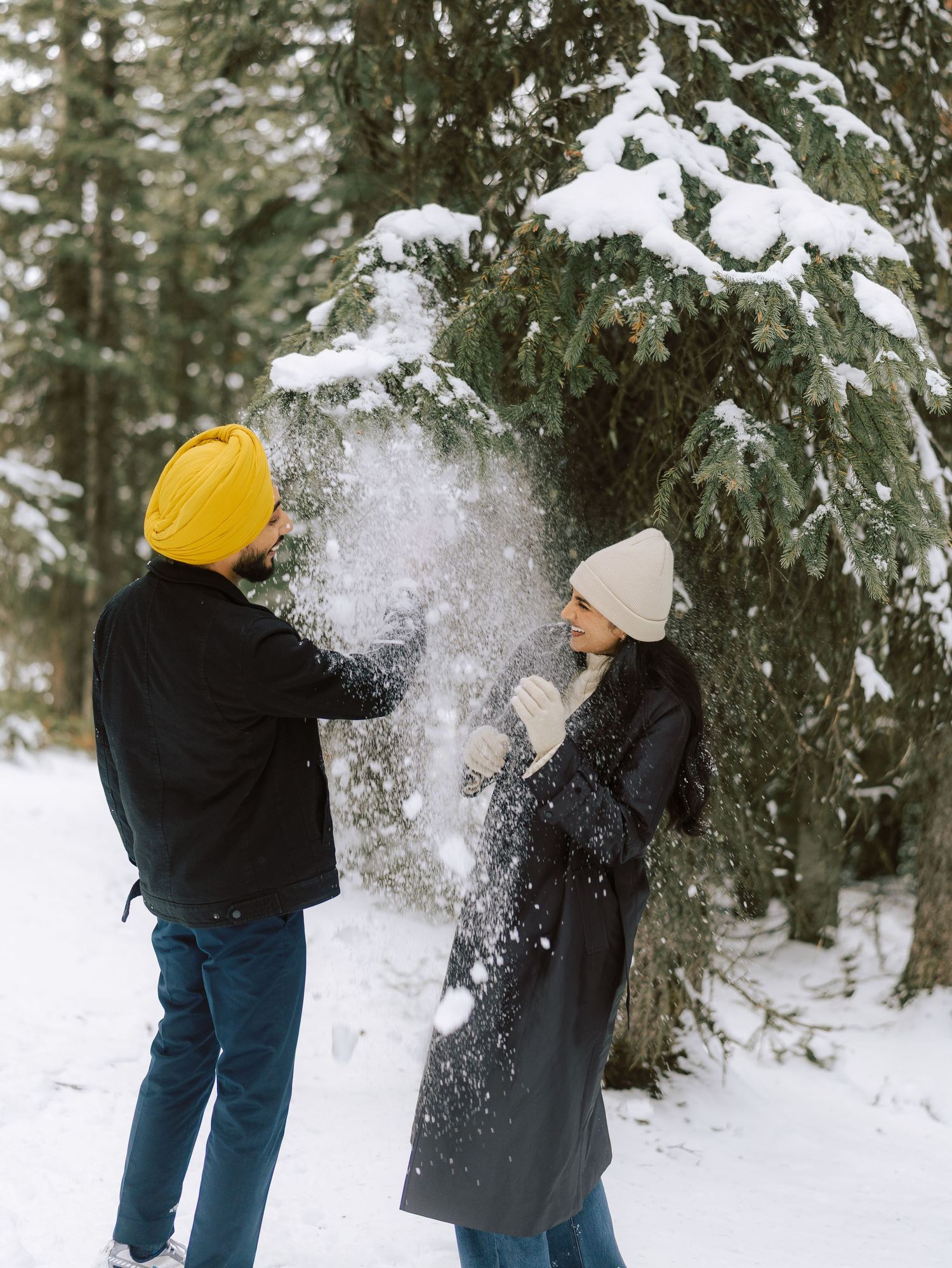 Couple having a playful snowball fight among snow-laden evergreen trees in a winter forest.