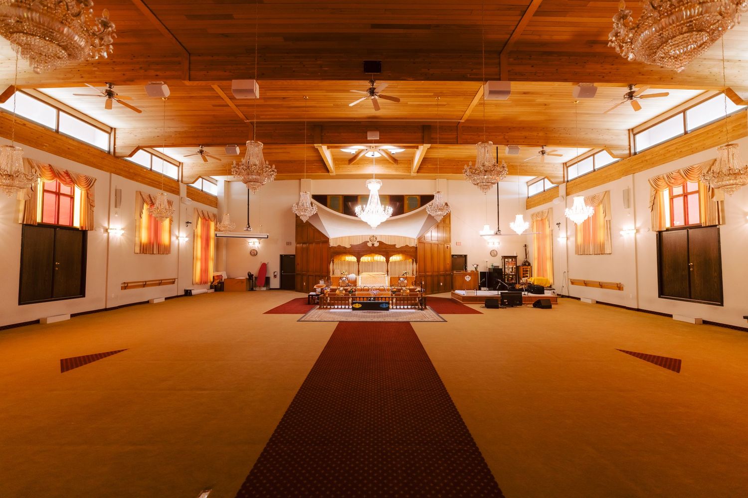 Elegant banquet hall with wood ceiling, chandelier, red carpet aisle, and warm amber lighting for events.