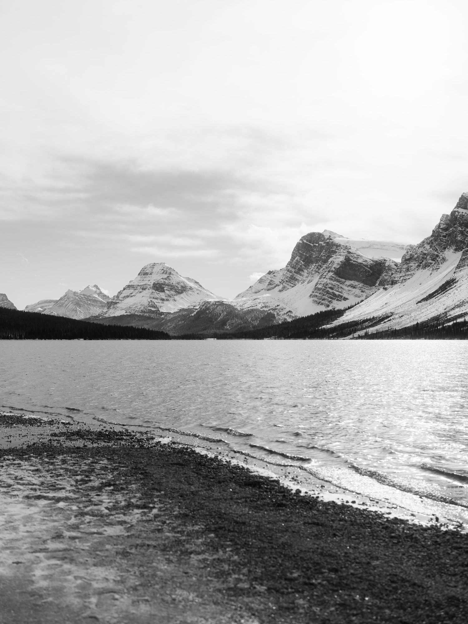 Black and white landscape of mountain lake with snow-capped peaks and rocky shoreline in Banff.