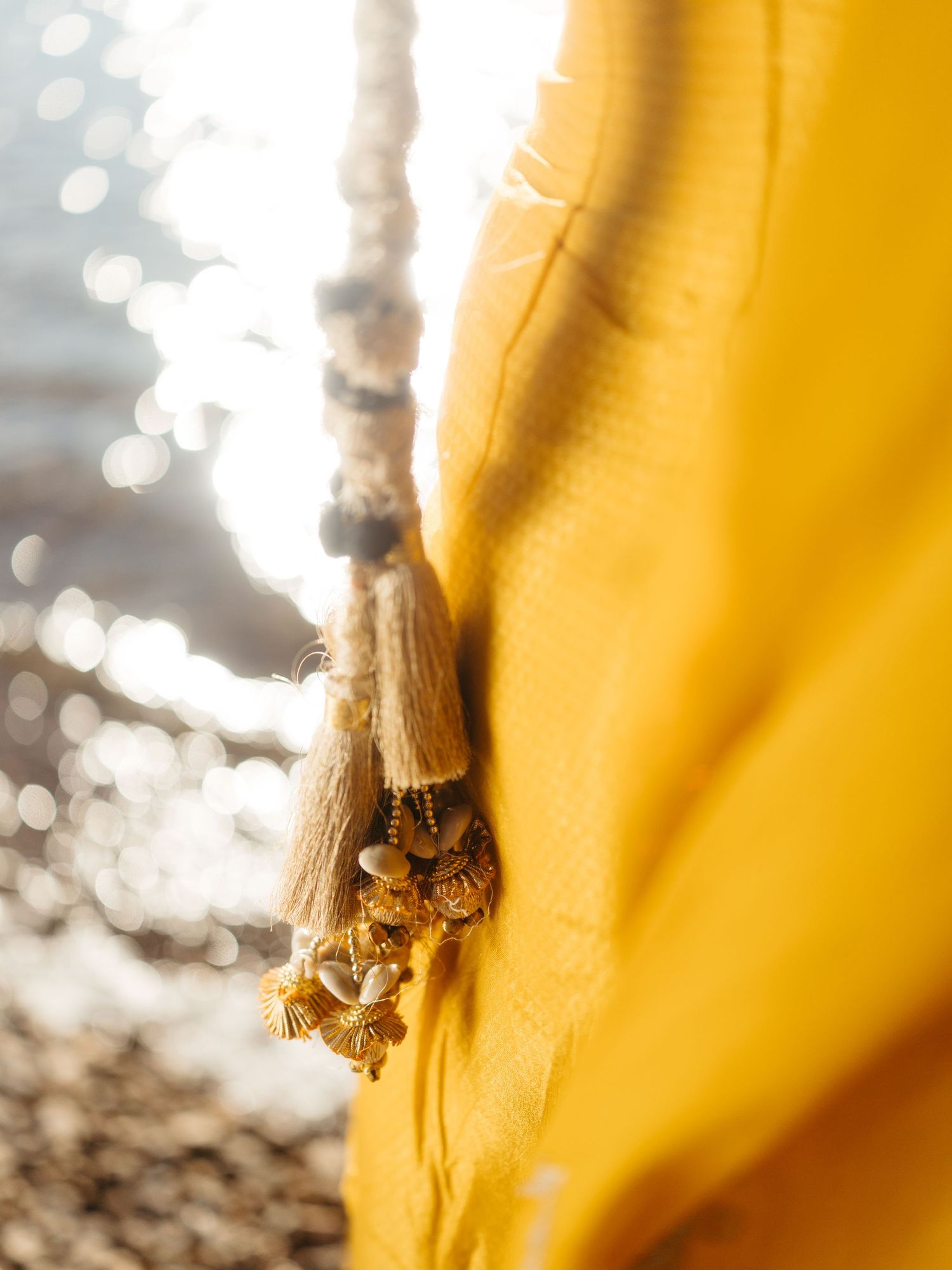 Close-up of golden yellow dupatta with decorative tassels and beaded embellishments in sunlight.