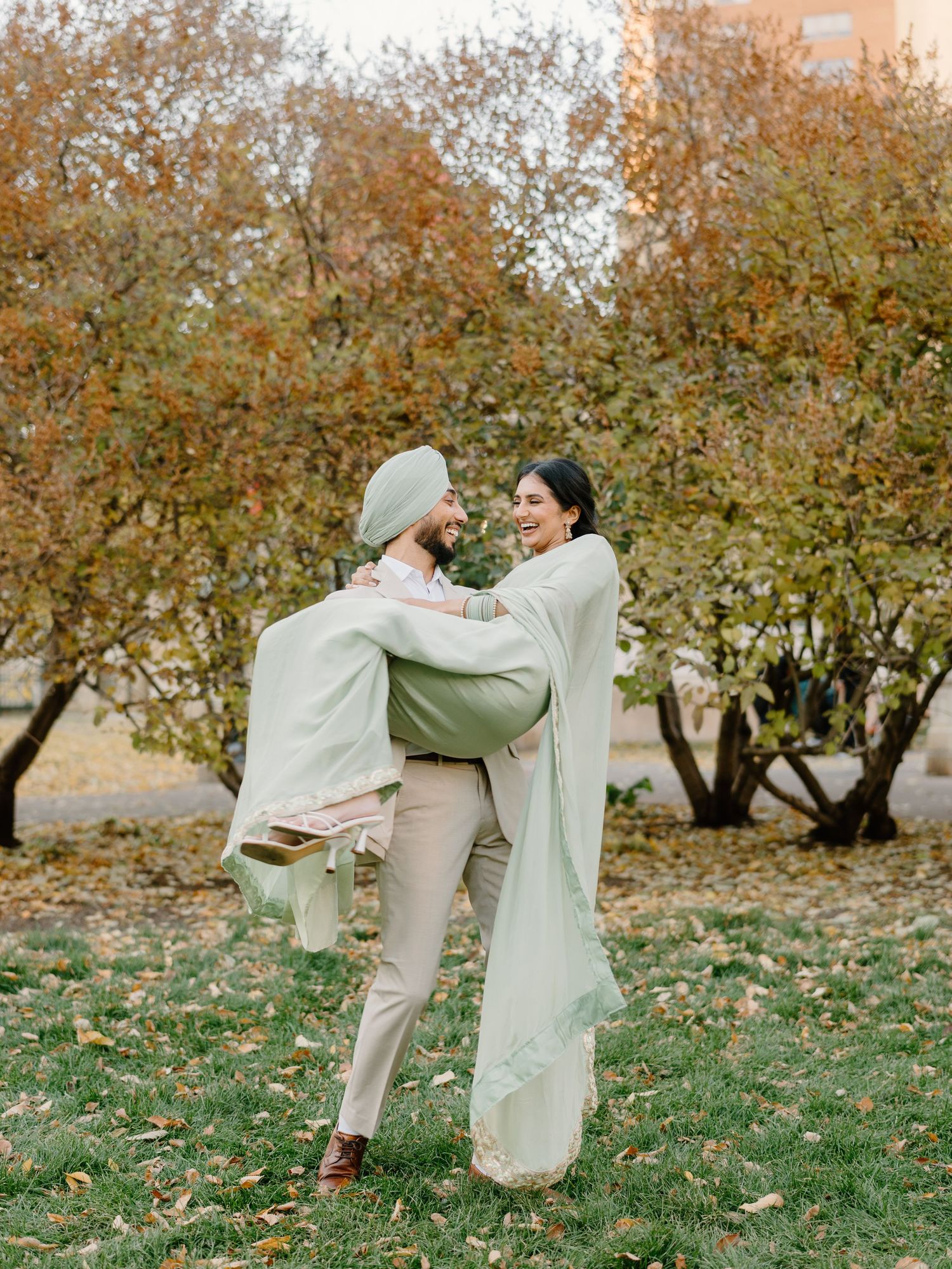 Sikh couple laughing and embracing outdoors wrapped in a flowing mint green saree dupatta.