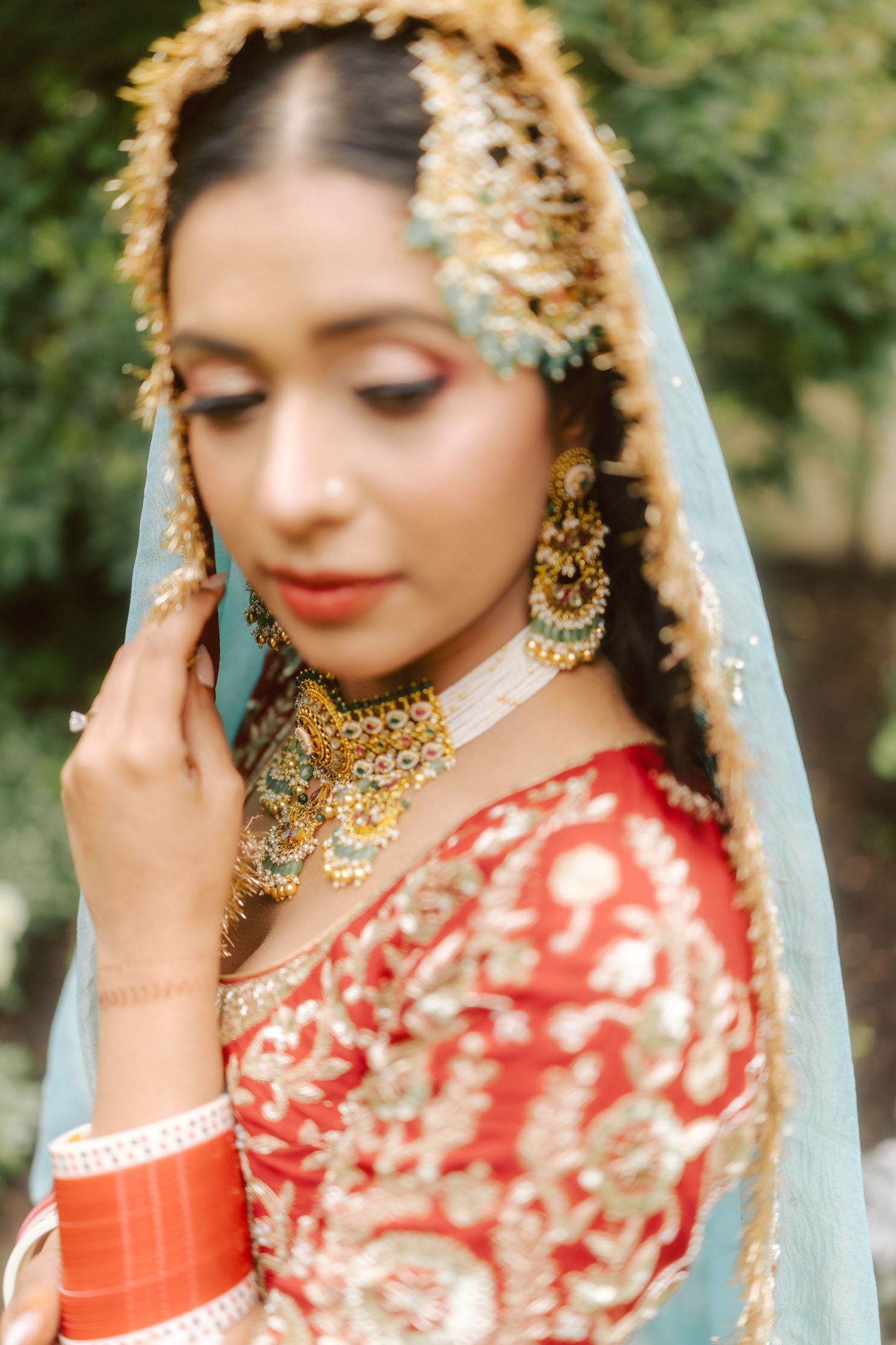 Close-up of Indian bride in red lehenga with gold jewelry and blue dupatta.
