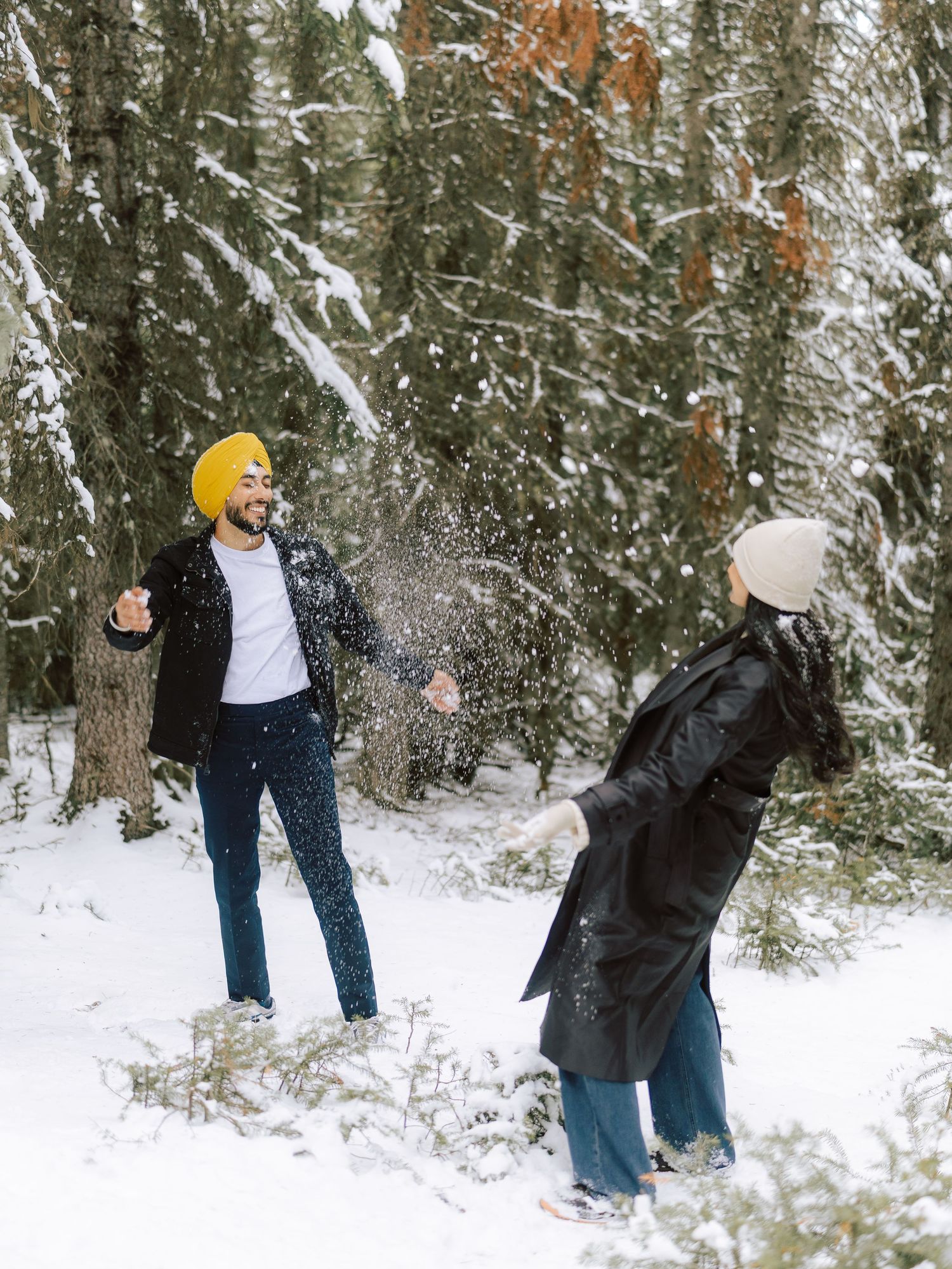 Laughing couple enjoying a snowball fight in a snow-covered evergreen forest in the Canadian Rockies.