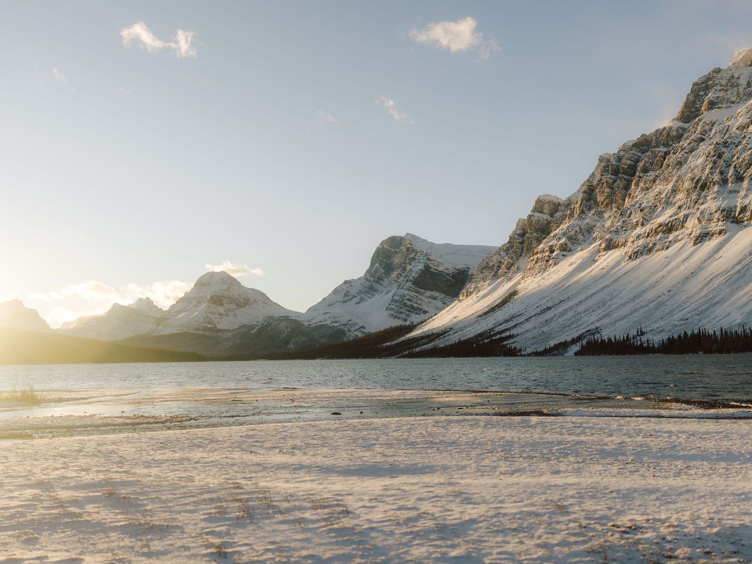 Golden sunset over frozen Bow Lake with dramatic snow-covered Rocky Mountain peaks in Banff National Park.