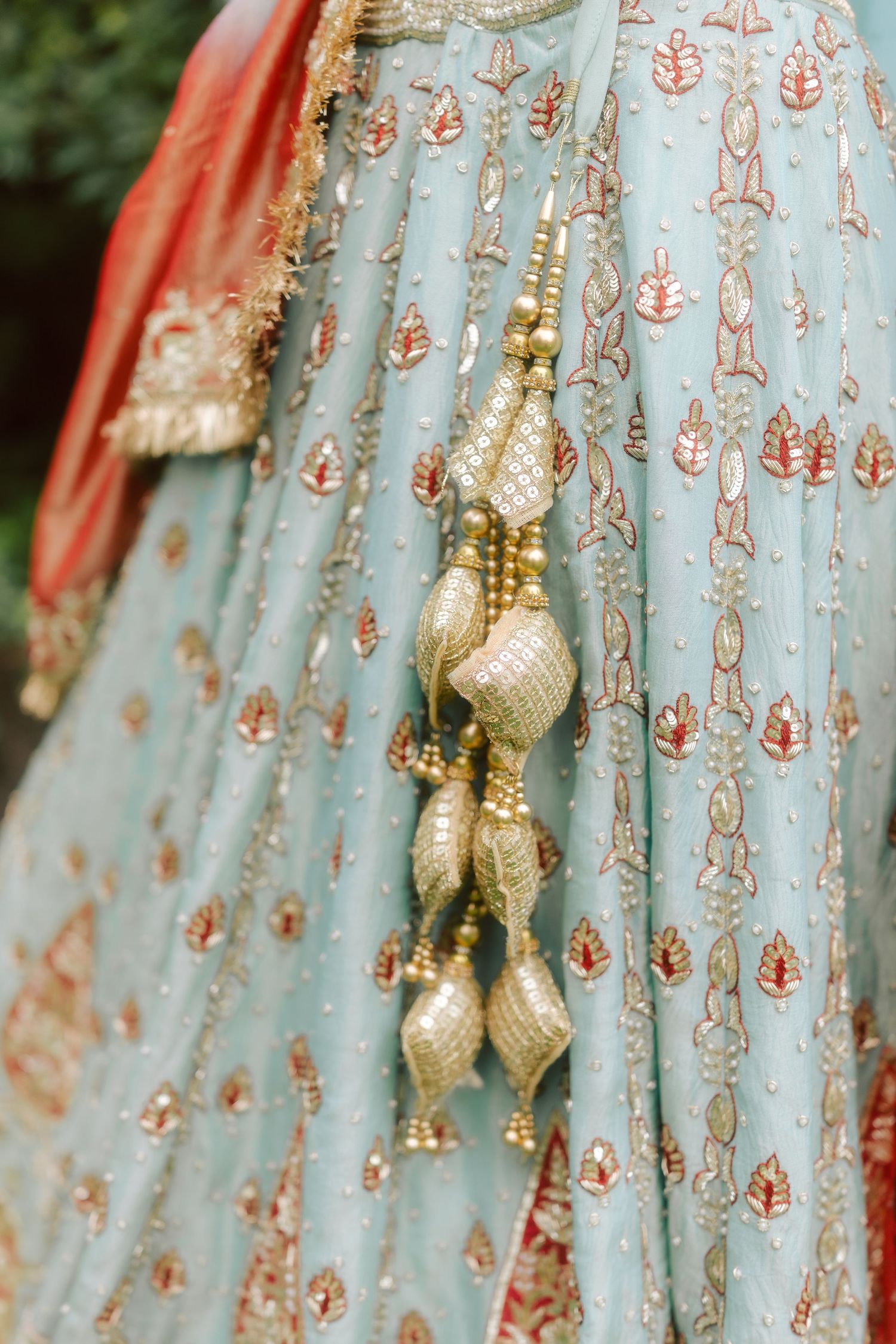 Close detail shot of gold embroidered kaleere charm hanging from Indian bridal blue lehenga dupatta.