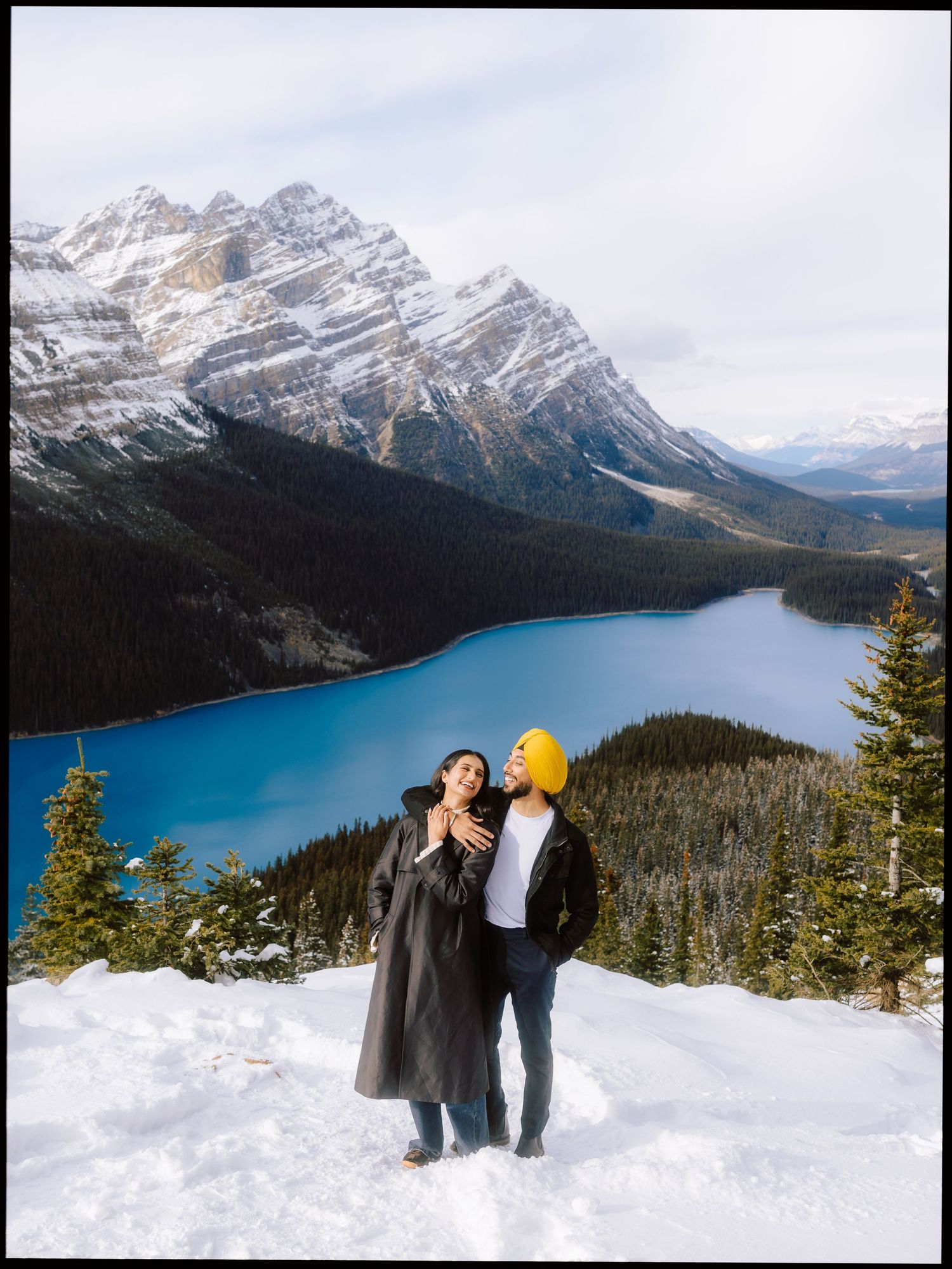 Couple posing in snow with stunning turquoise Peyto Lake and Canadian Rockies behind them.