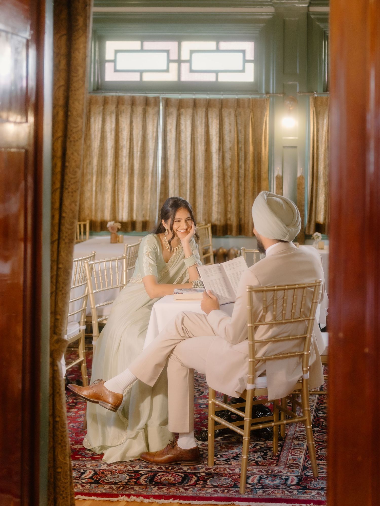 Sikh couple sharing an intimate moment seated in an elegant gold and green decorated wedding venue.