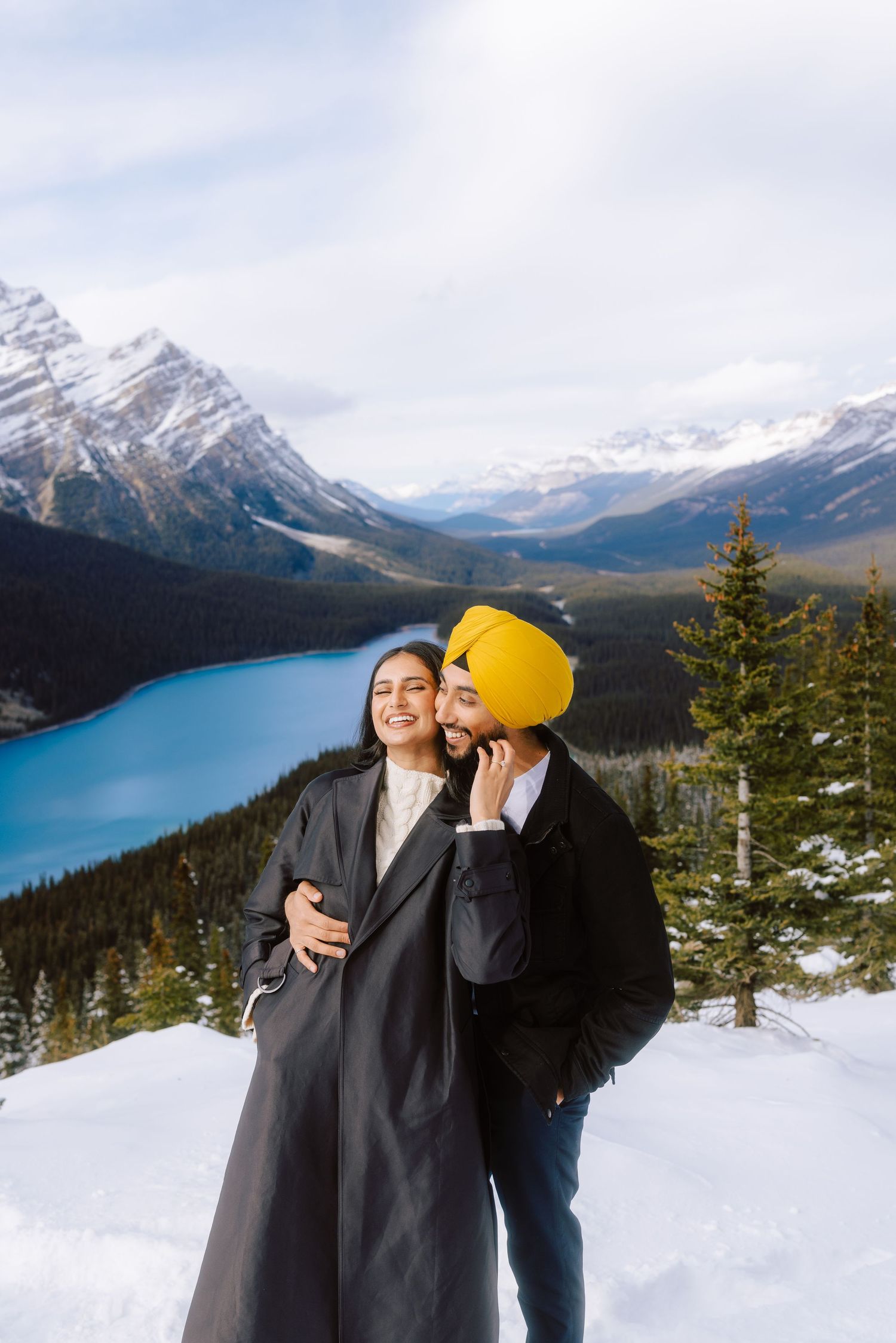 Couple posing at snowy Peyto Lake overlook in Banff, man wearing yellow turban kissing womans cheek.