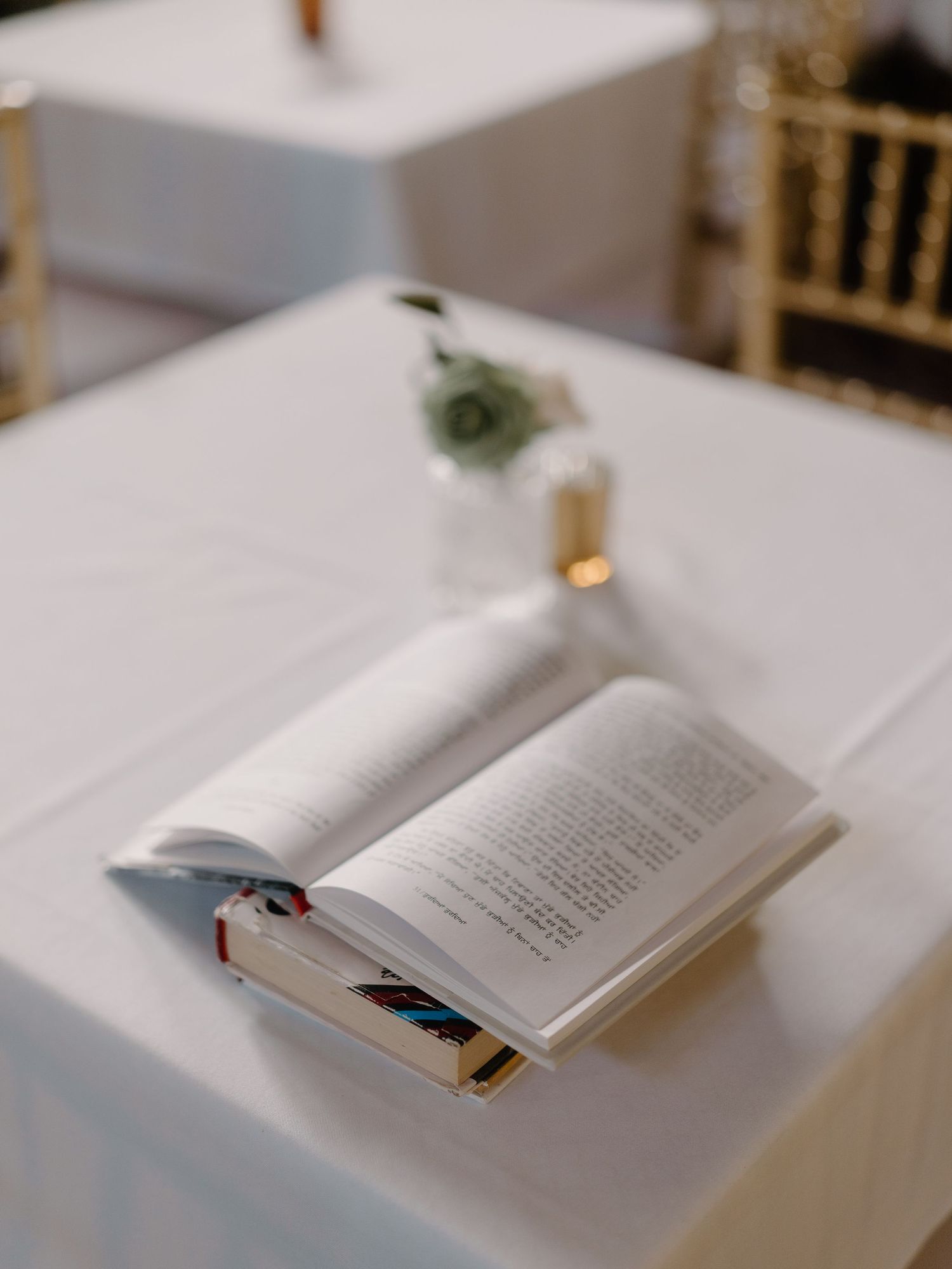 An open book rests on a white tablecloth beside a small floral arrangement at a wedding reception.