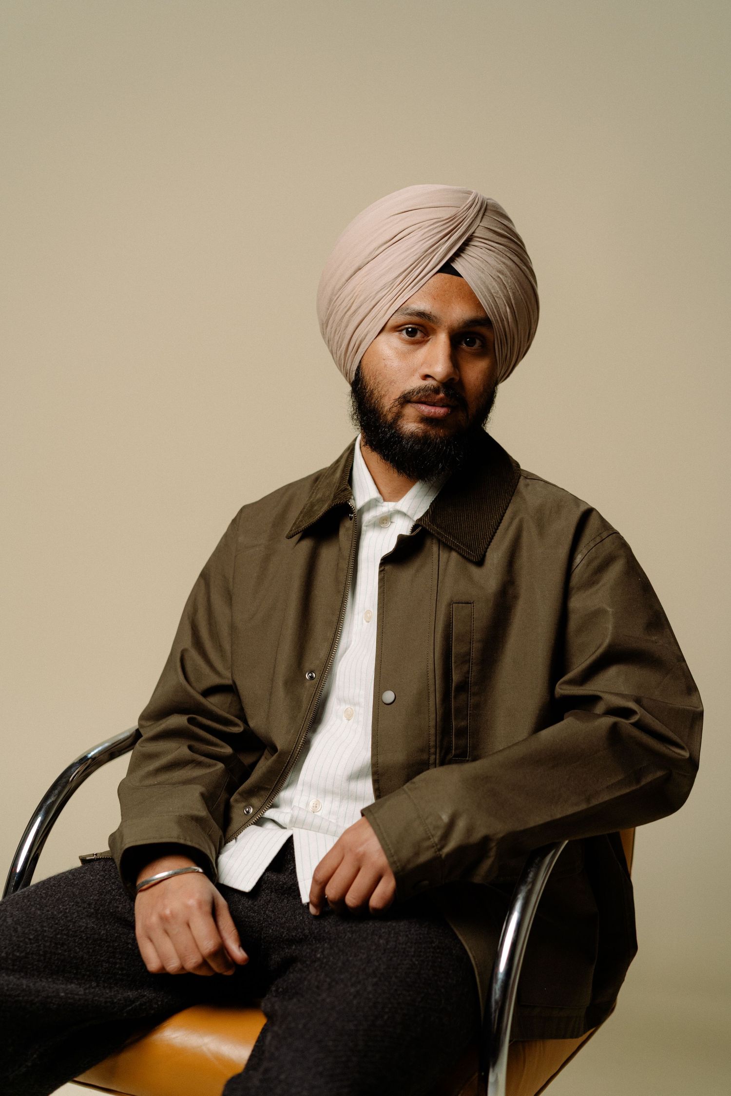 Bearded Sikh man in pink turban and olive jacket sits confidently on a leather chair.