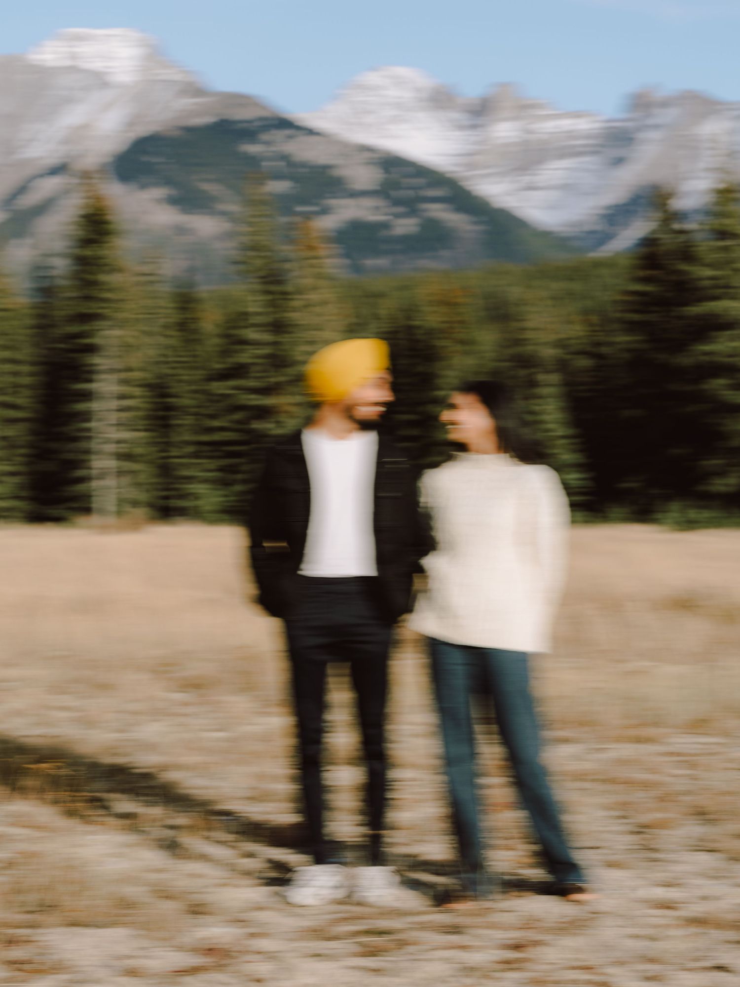 Intentionally blurred artistic photo of couple standing together in mountain meadow with Rockies backdrop.