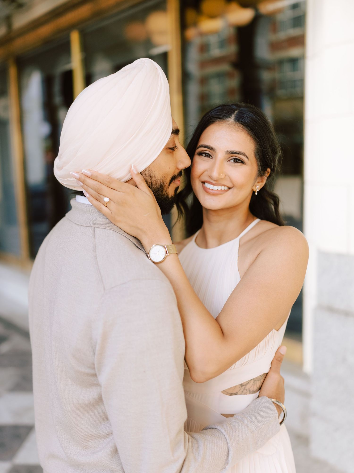 Bride smiles warmly while embracing groom wearing a pink turban during engagement shoot.
