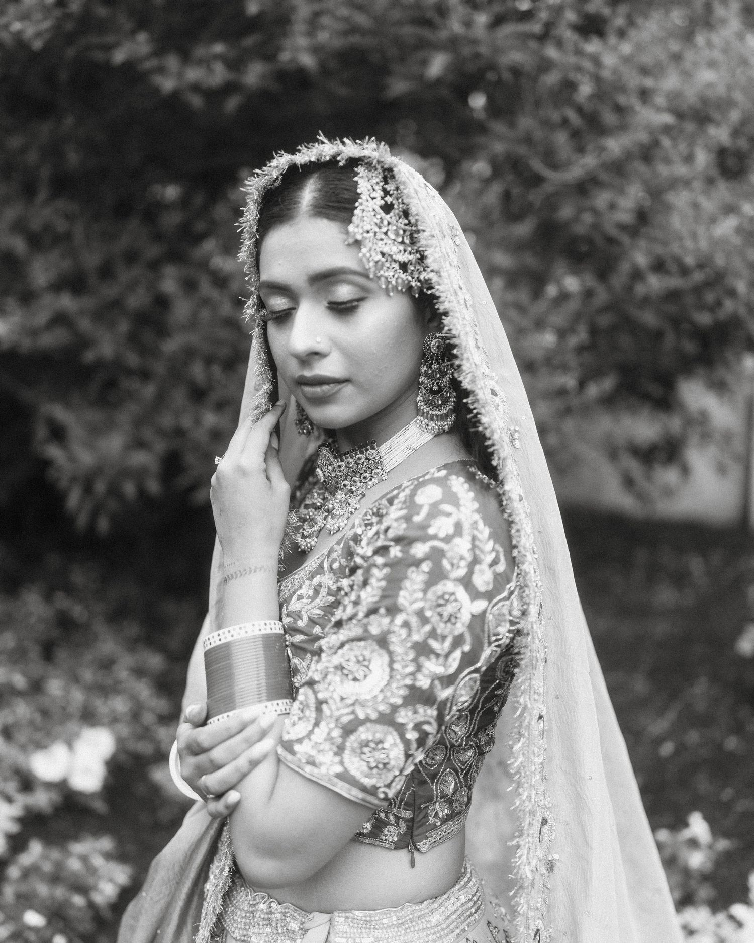 Black and white portrait of Indian bride in embroidered lehenga with ornate headpiece and veil.