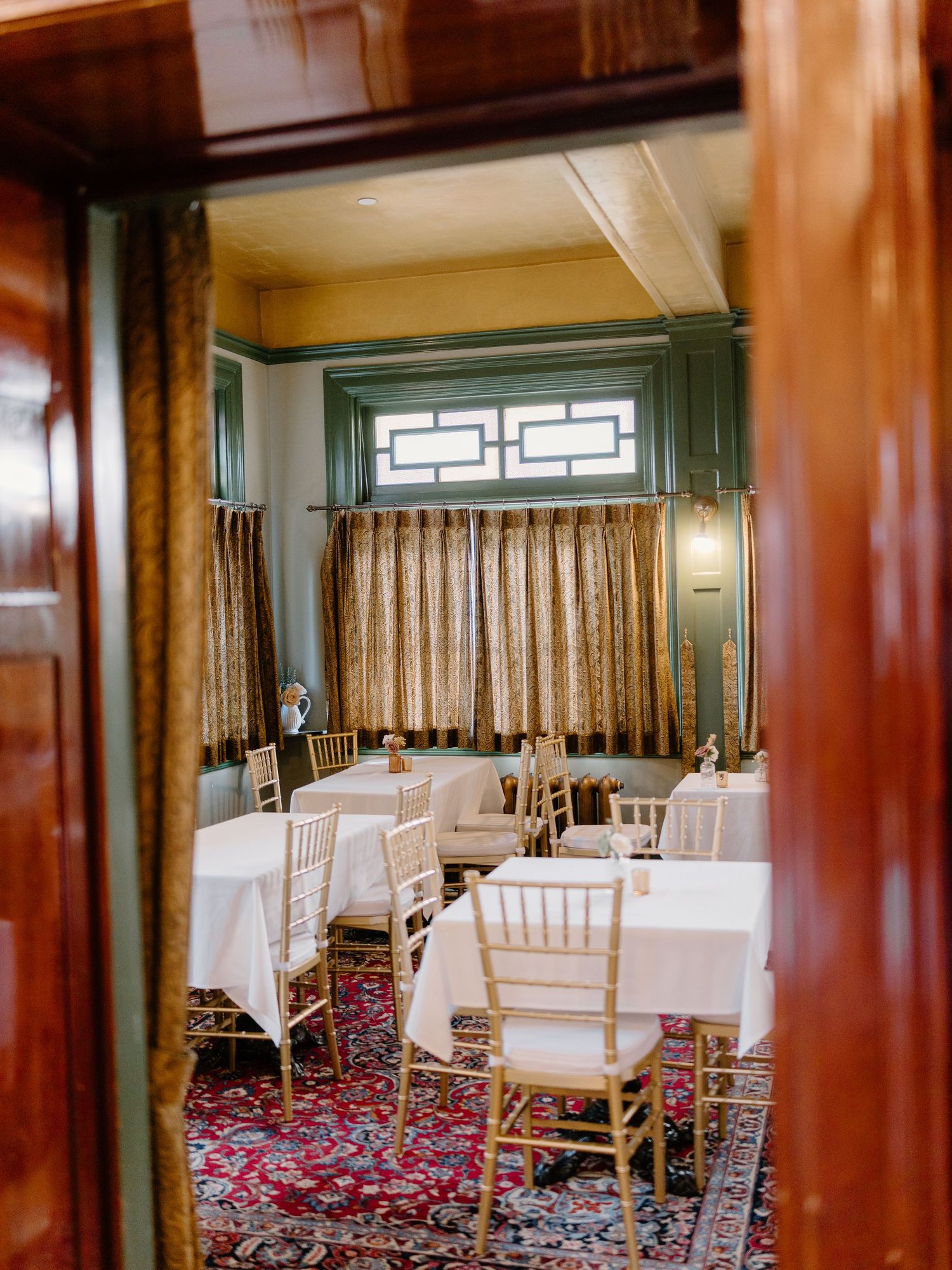 Elegant wedding reception room with gold chiavari chairs and white tables viewed through wooden doors.