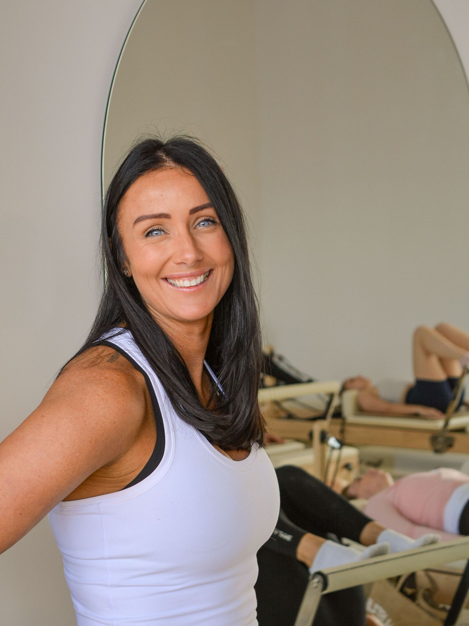 Woman in white tank top smiling while sitting at desk in classroom setting.