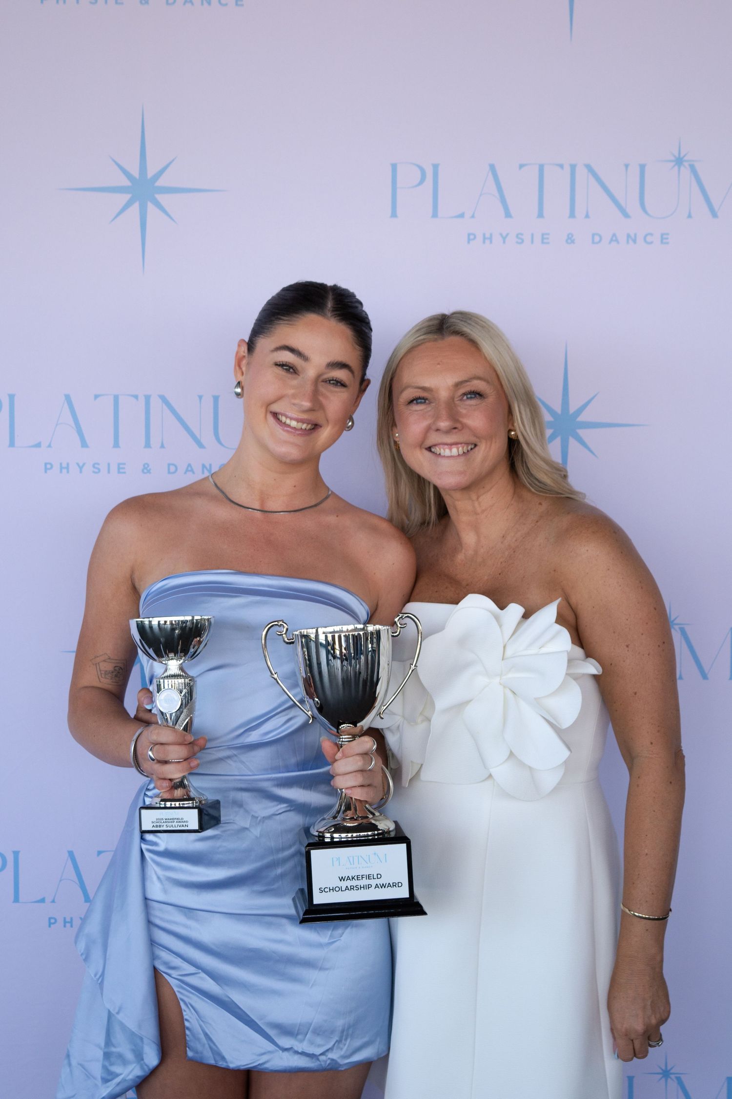 Two people pose with trophy awards against a Platinum branded backdrop.
