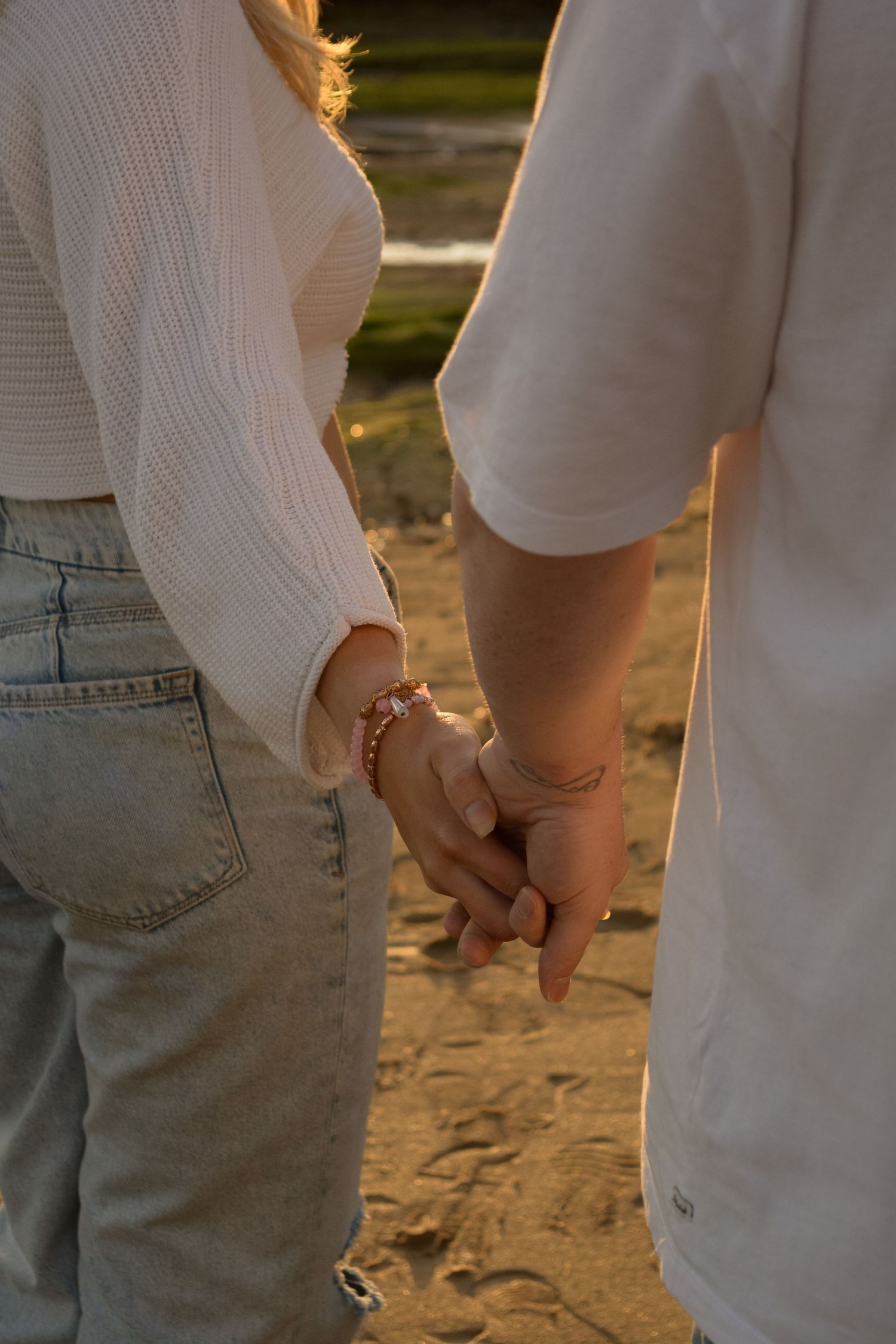 Close-up of couple holding hands at sunset with soft golden lighting.