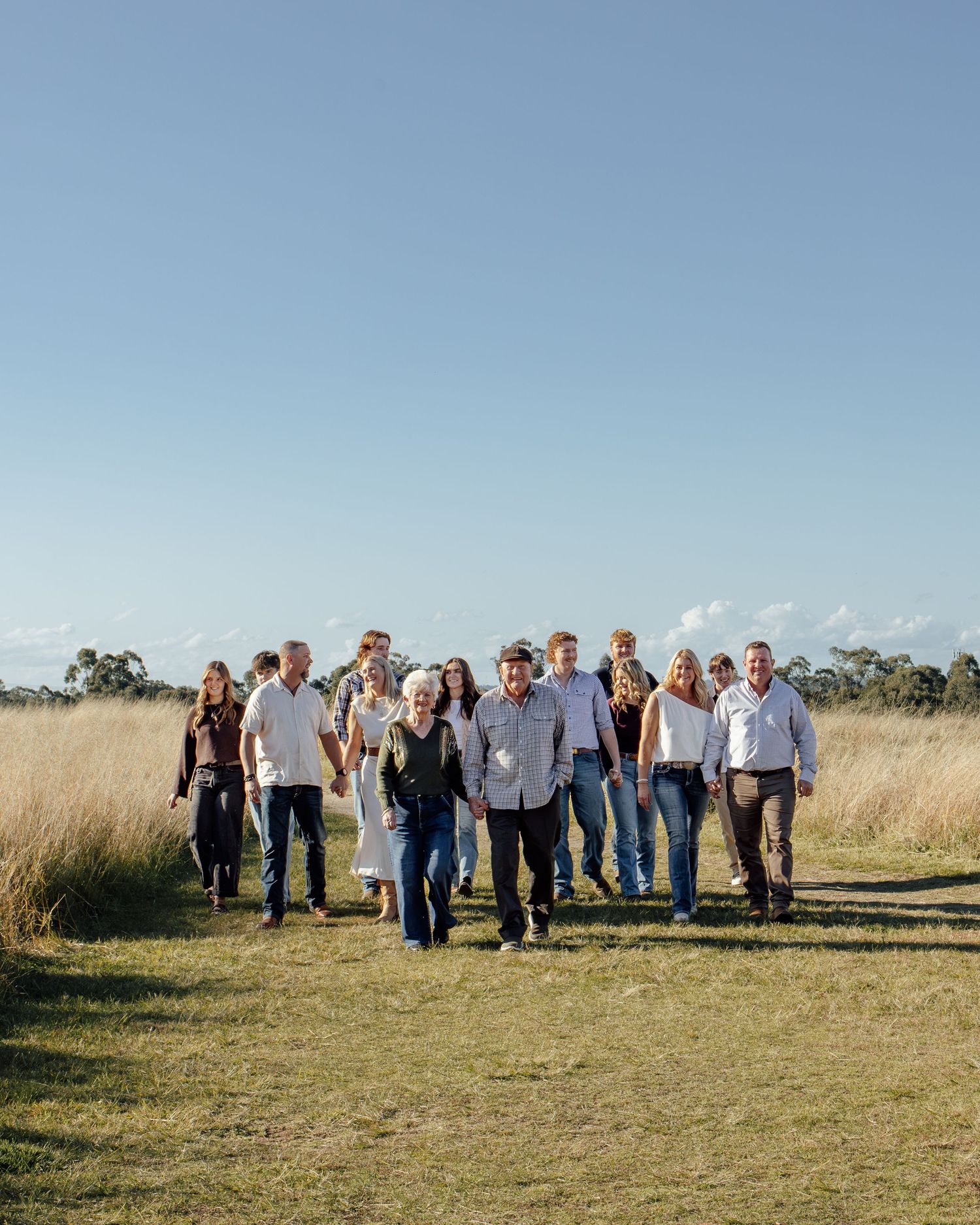 Large family group walking together through an open grassy field under a clear blue sky on a sunny day.