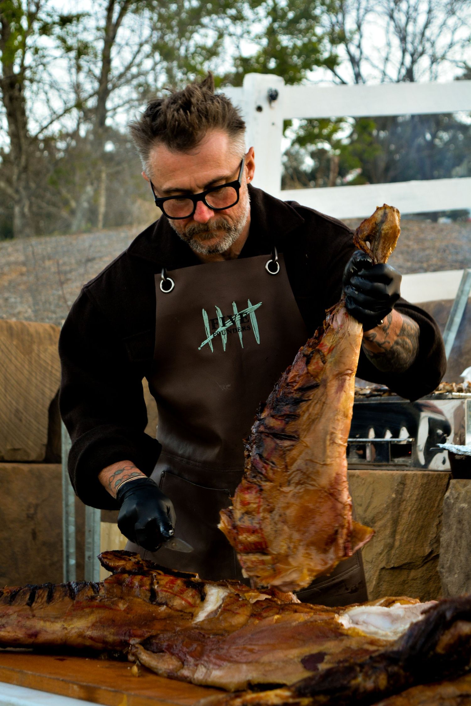 Chef skillfully carving a large piece of smoked meat on a wooden cutting board.