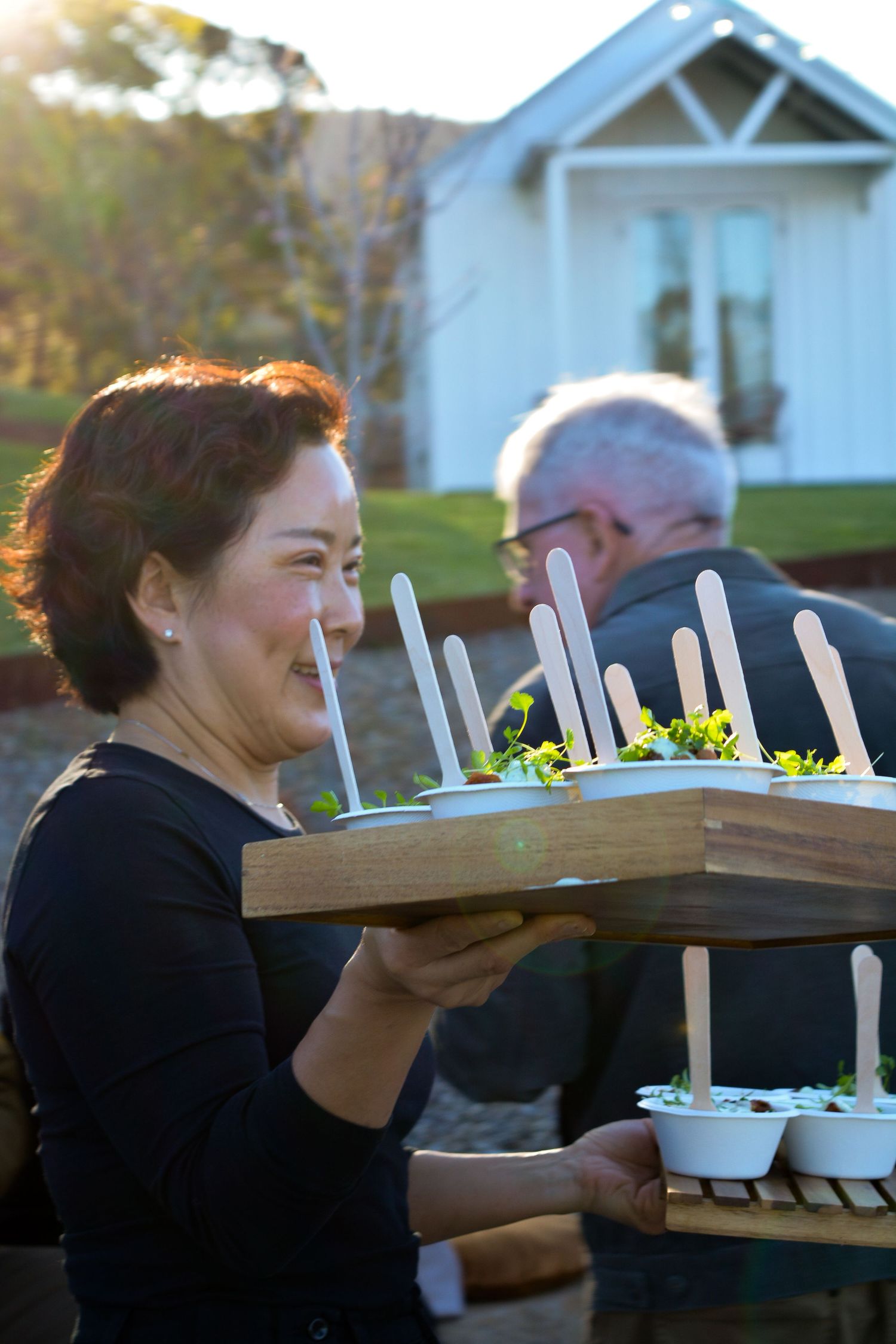 Server carrying wooden serving boards with appetizers at an outdoor event.