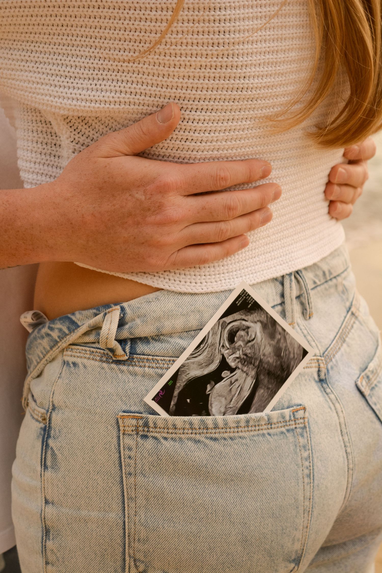 Close-up of hands placing something in back pocket of light wash denim jeans.