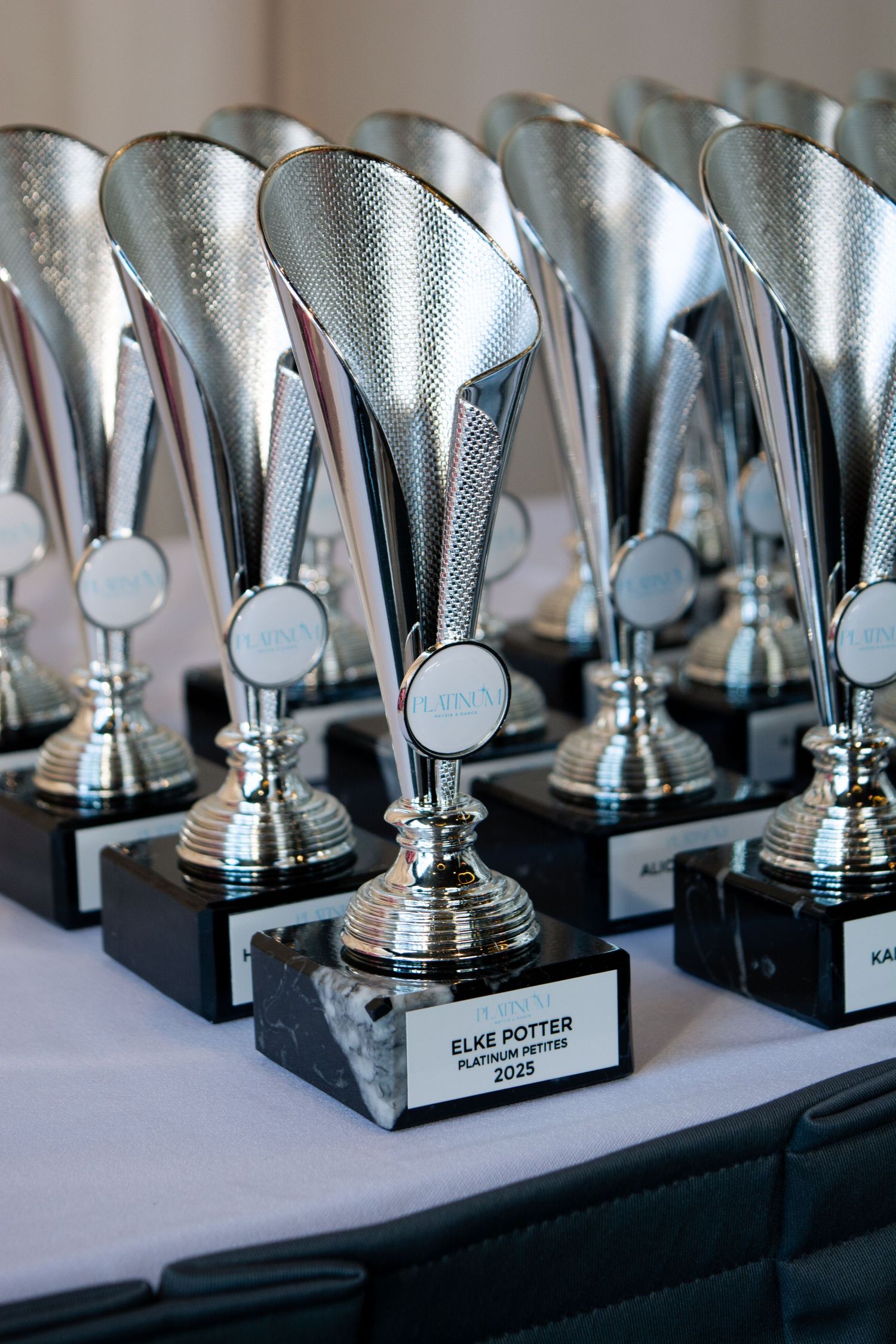 A row of silver trophy awards displayed on a black table.