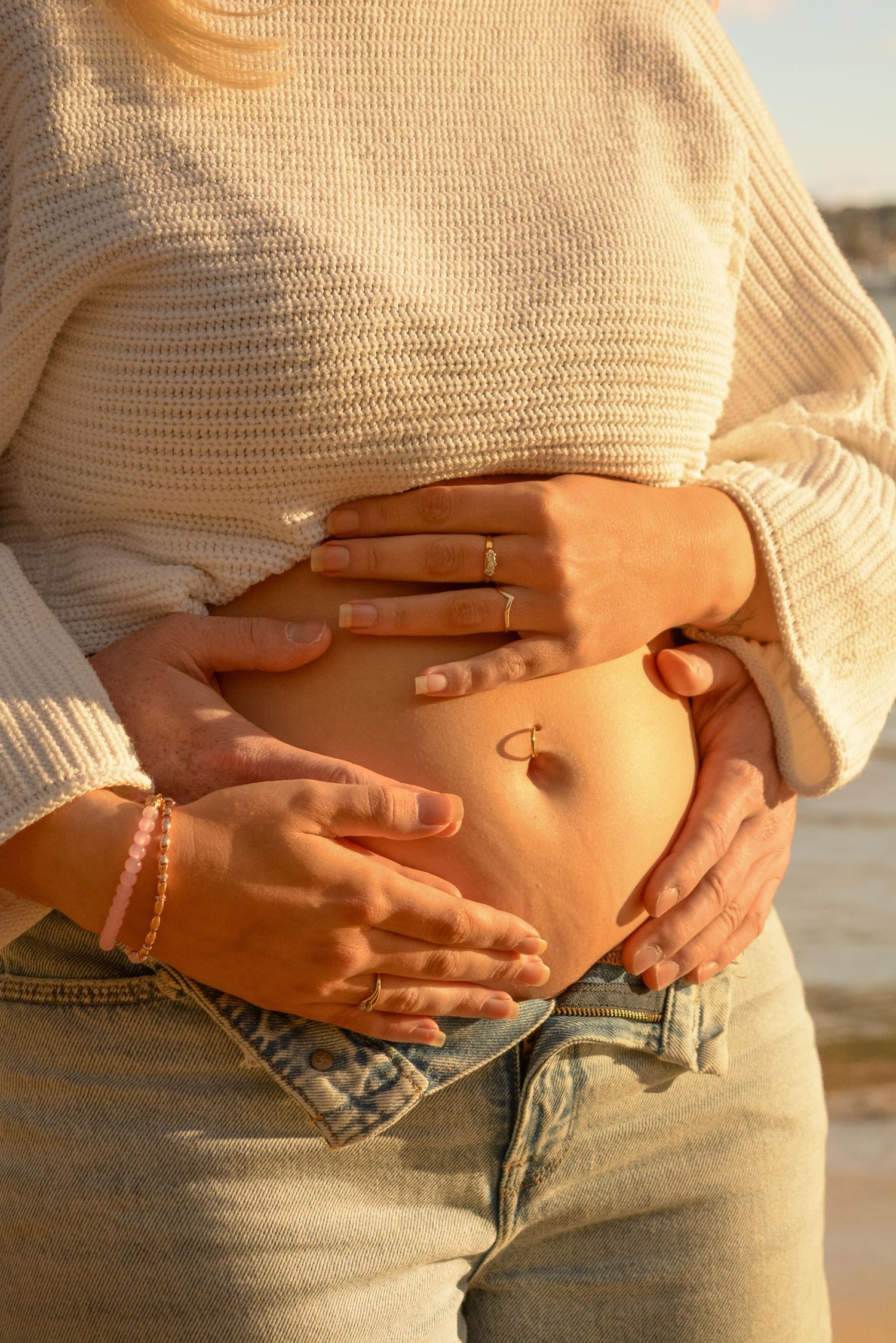 Close-up shots of a pregnant belly in a cream sweater against a sunset backdrop.