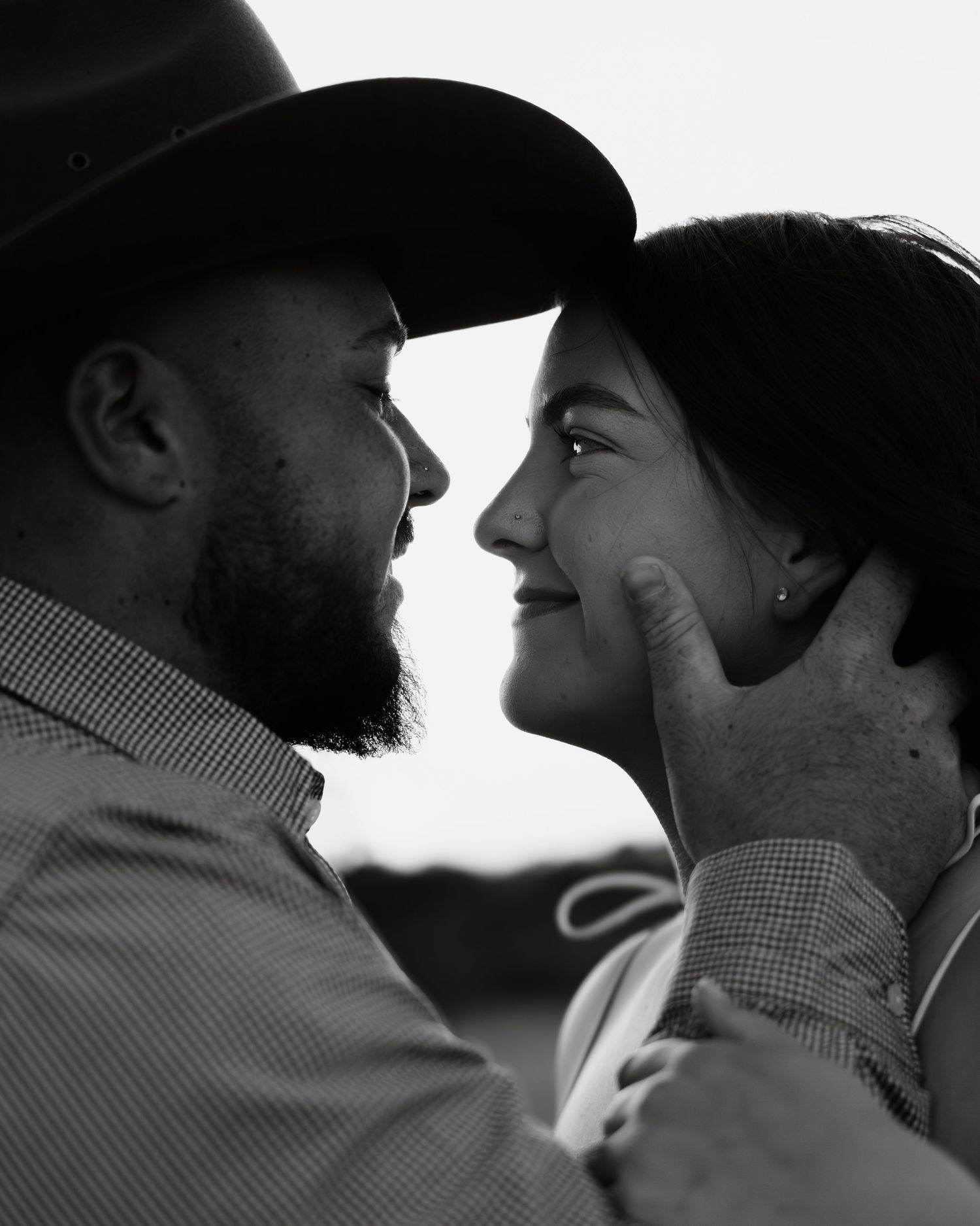 Black and white photo of a bearded man in a cowboy hat tenderly cupping a smiling woman's face in a romantic moment.