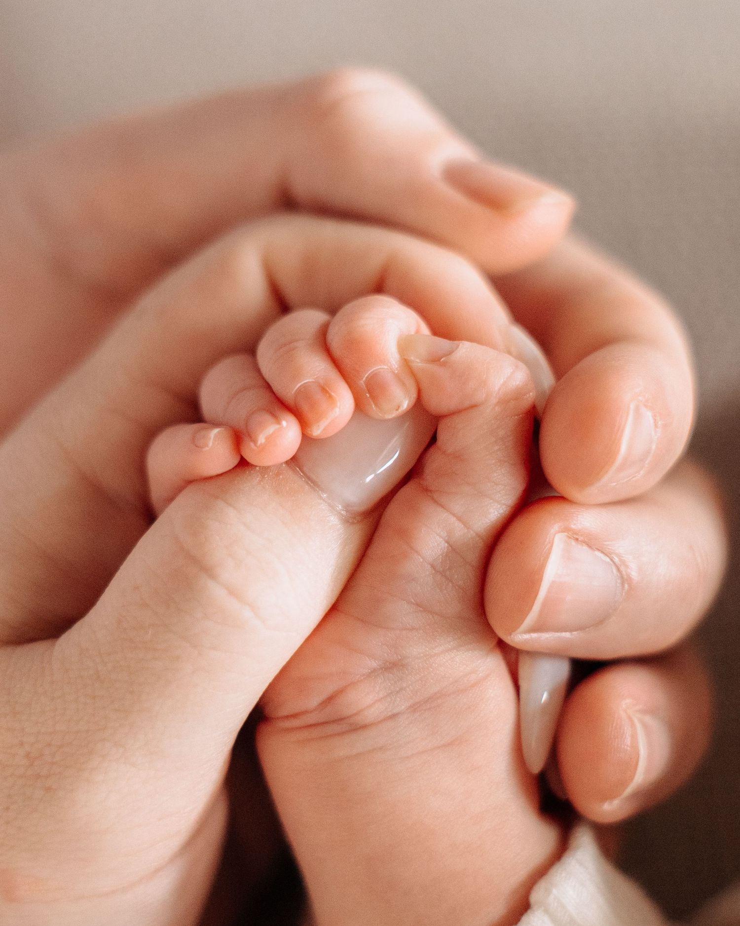 Close-up of a newborn baby's tiny hand gently gripped by two adult hands, symbolizing love and protection.