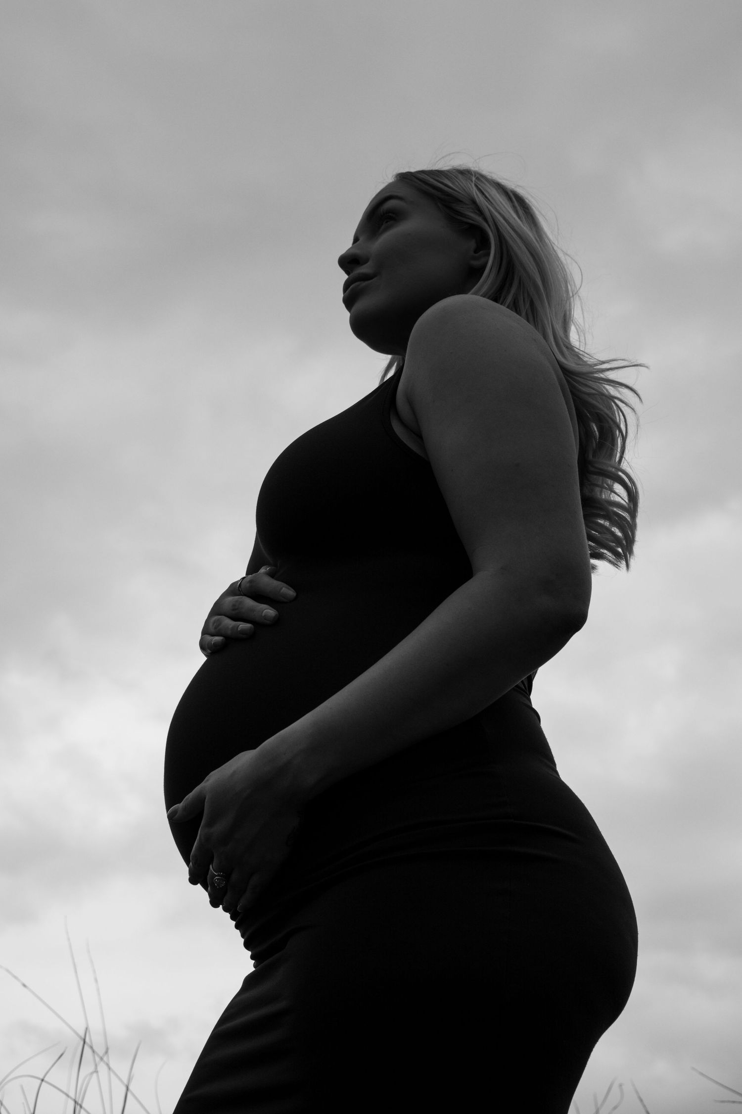 Black and white silhouette series showing pregnancy progression against cloudy sky background.