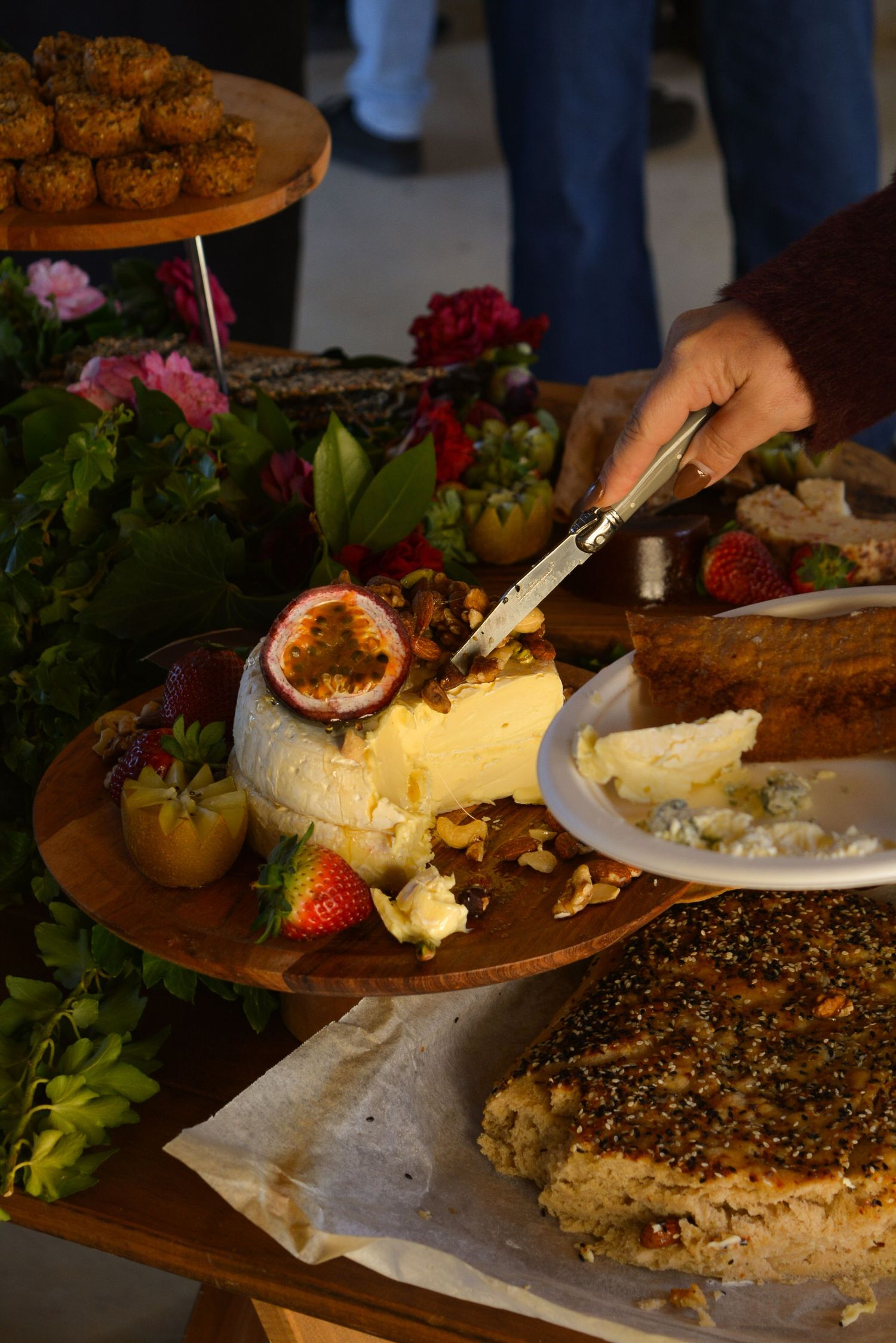 Hands serving cheese and appetizers on wooden boards with floral decorations.