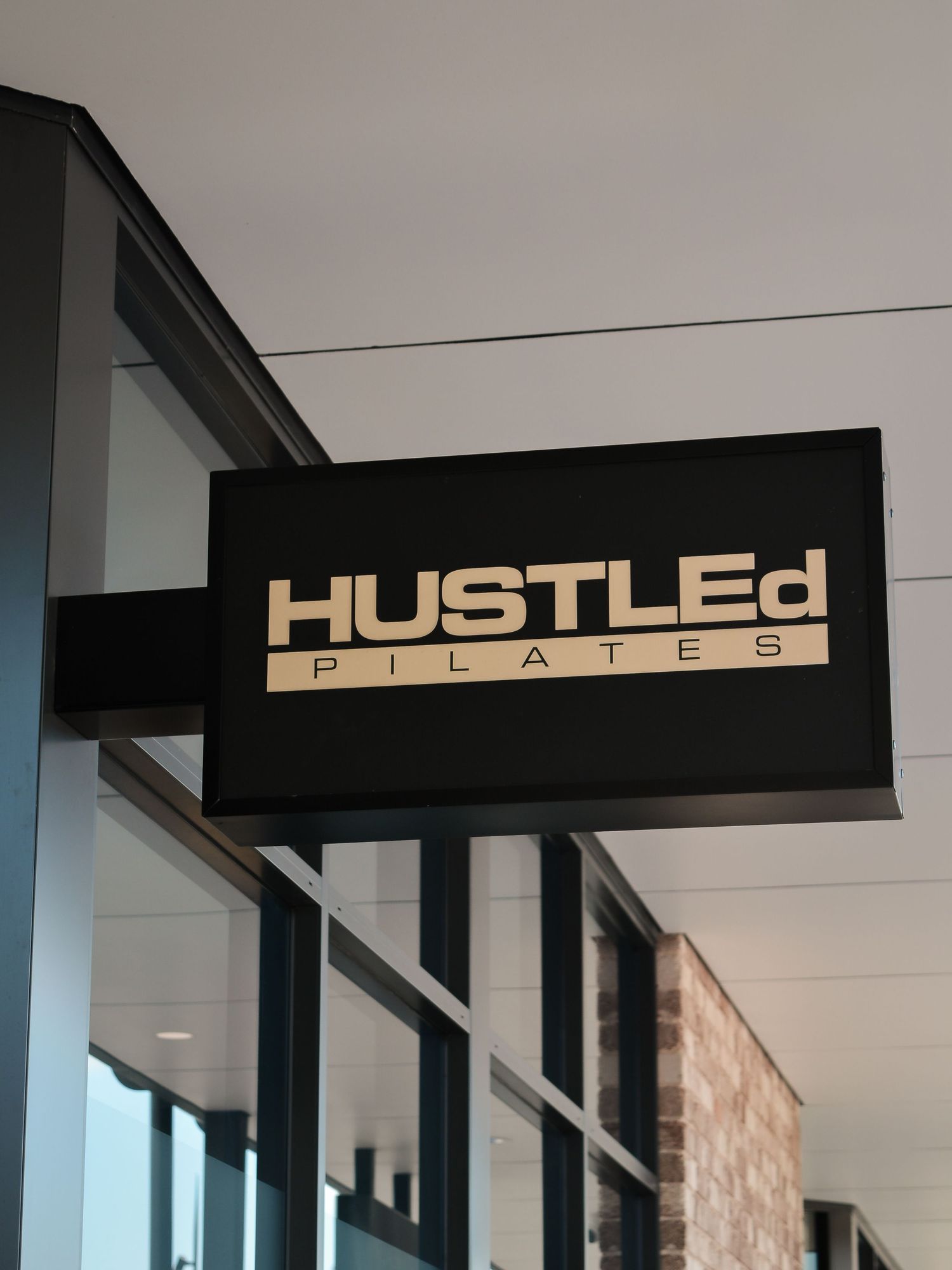 Black storefront sign displaying 'HUSTLEd PILATES' in gold lettering against a modern building exterior.