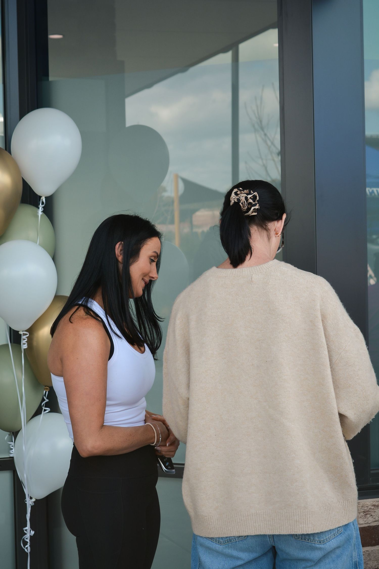 Group of people standing near windows decorated with white balloons at an indoor event.