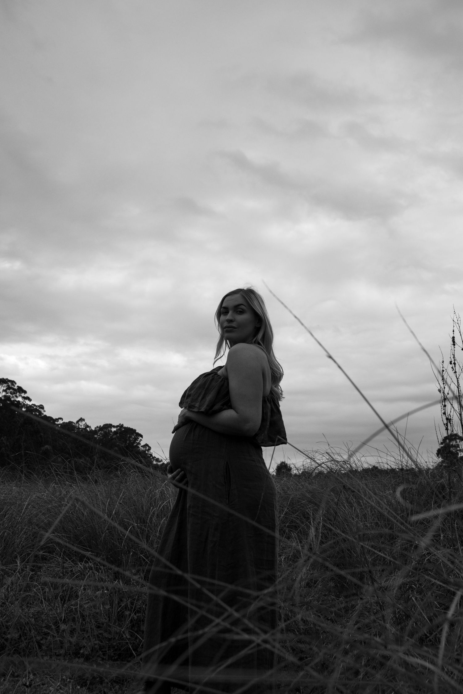 Moody black and white sequence showing figure in dark clothing standing against cloudy sky in field of tall grass.