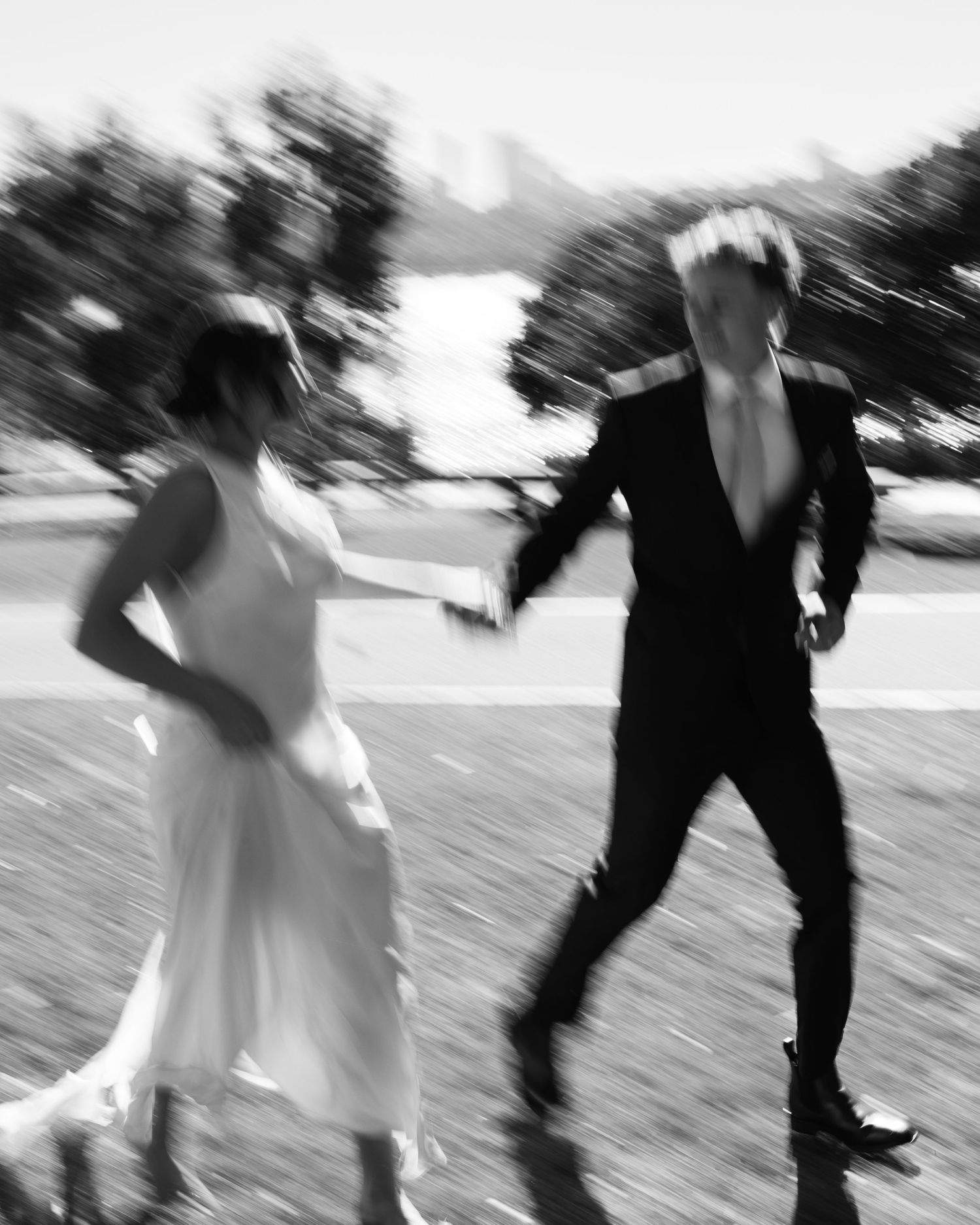 Blurred black and white photo of bride and groom running together outdoors on their wedding day.