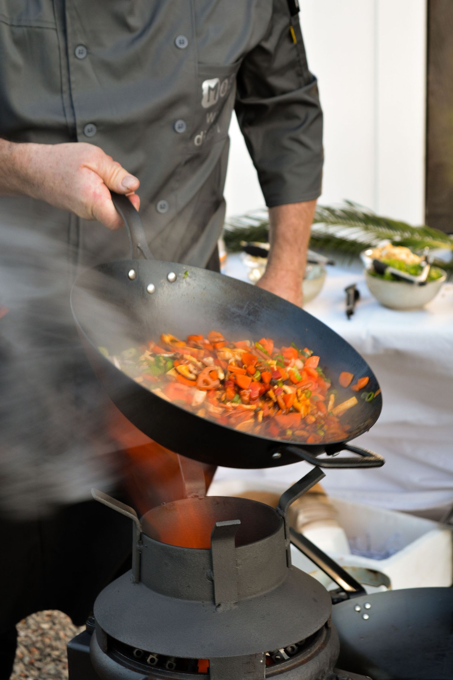 Chef stir-frying vegetables in a wok over a gas flame.