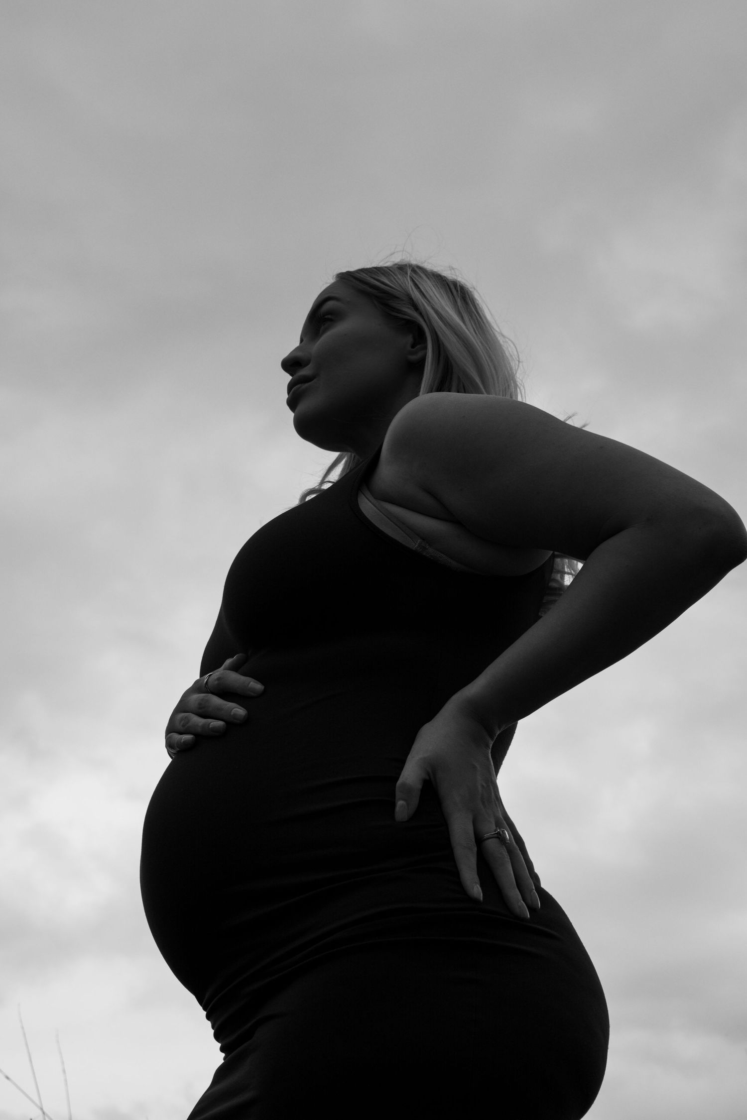 Dramatic black and white silhouette of a pregnant woman against a cloudy sky.