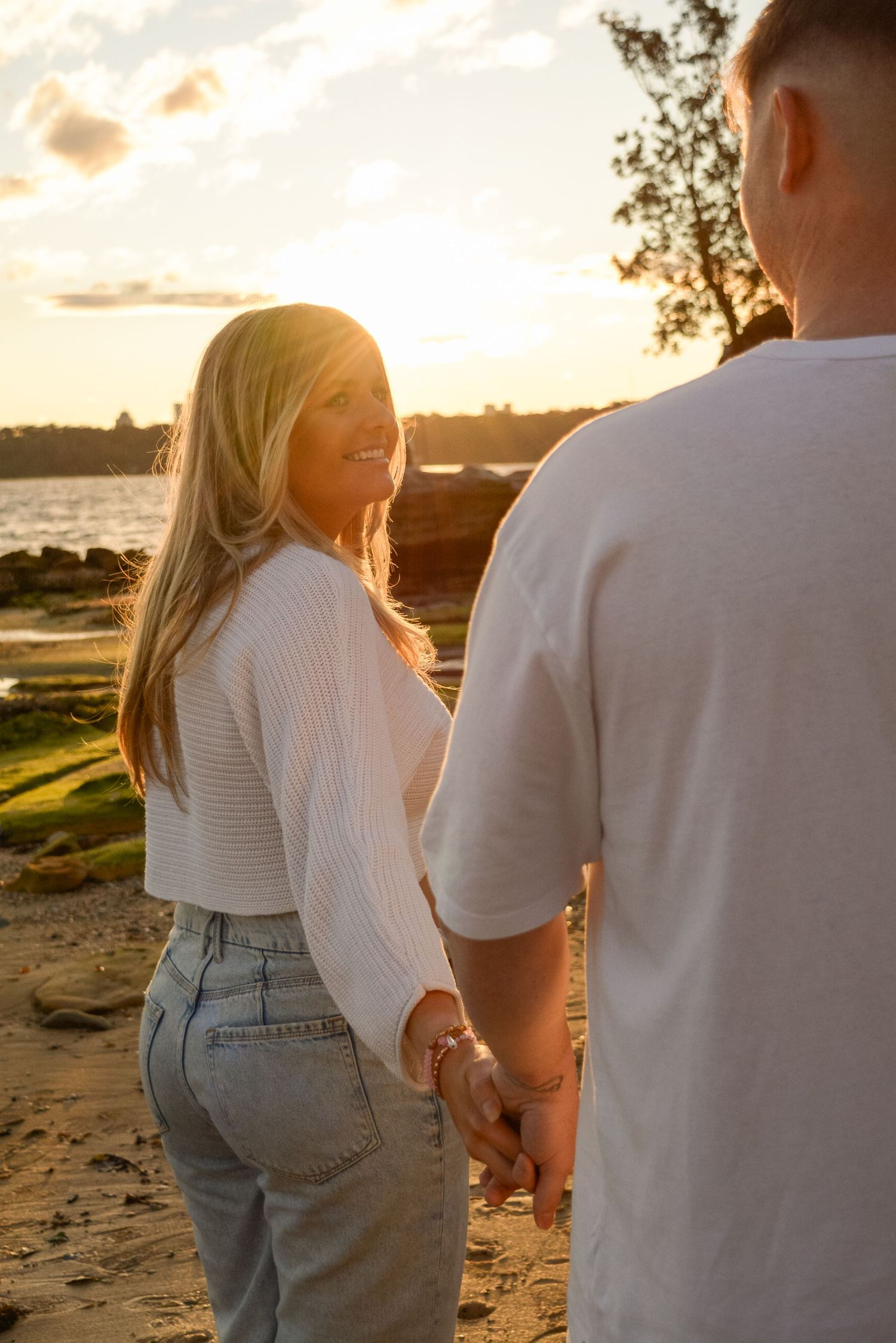 A couple walking together on a beach at golden hour wearing casual outfits.