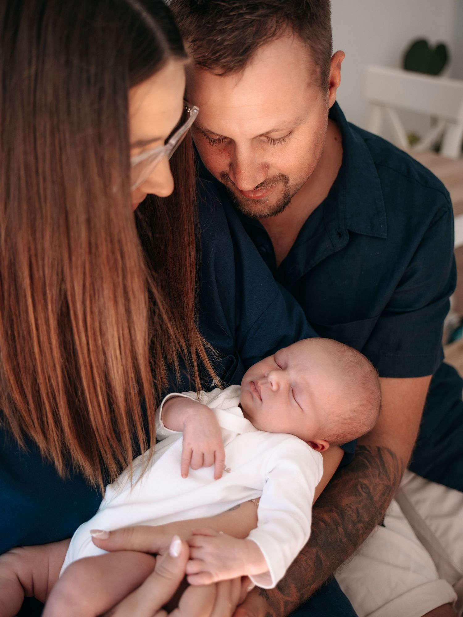 Parents lovingly gazing at their sleeping newborn baby dressed in white, sharing a tender family moment.