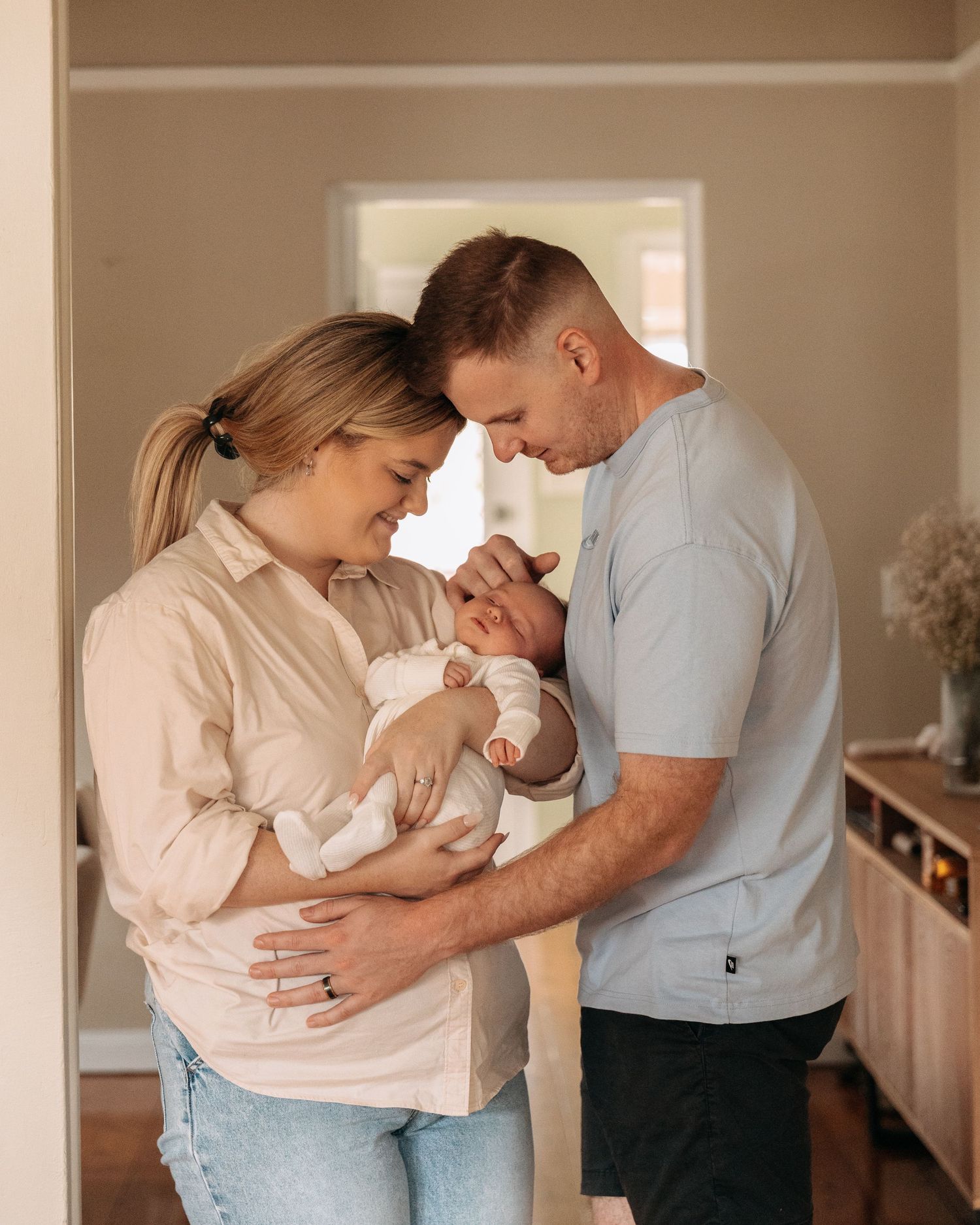 Happy couple smiling at their newborn baby held in mothers arms inside their home.