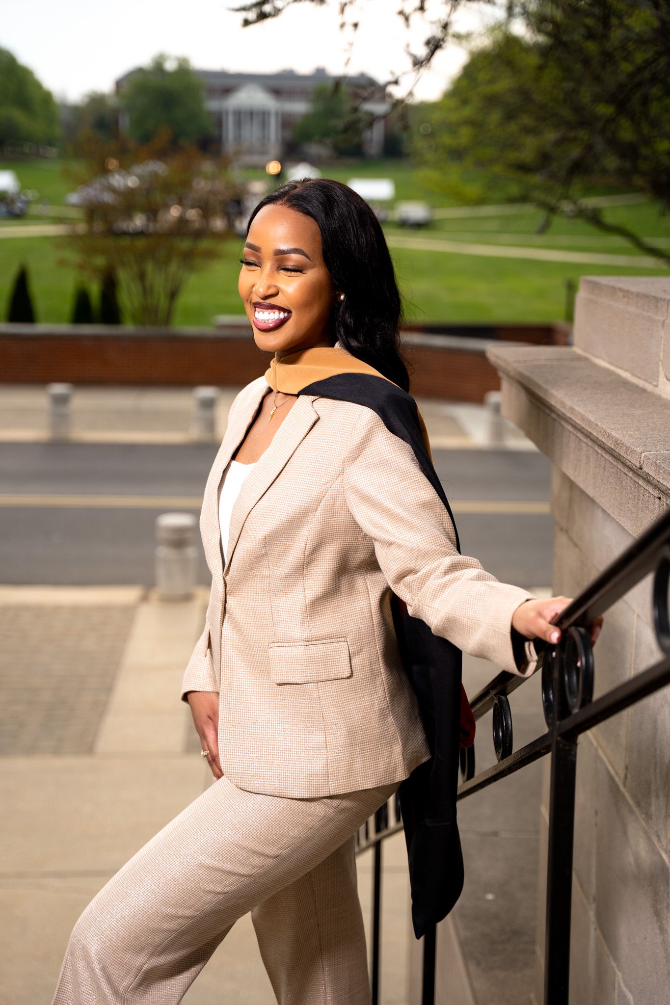 Graduate in cream colored suit poses confidently on outdoor steps.